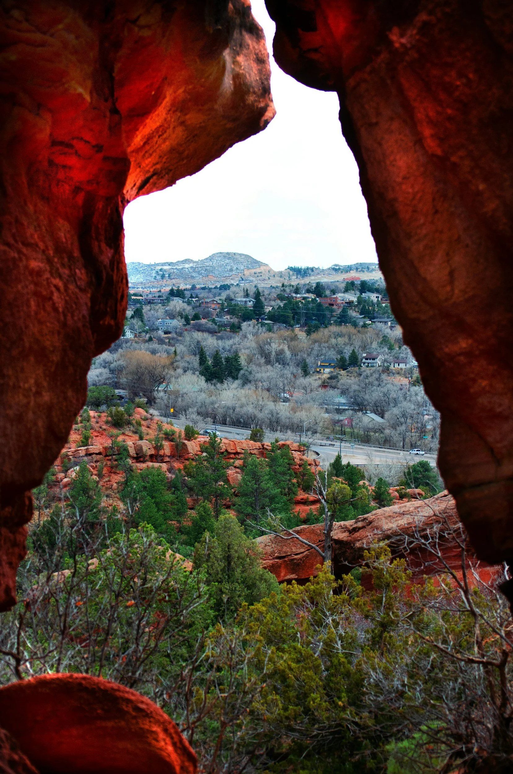 View of a hilly residential area with trees and houses, framed by the natural opening of reddish rocks.
