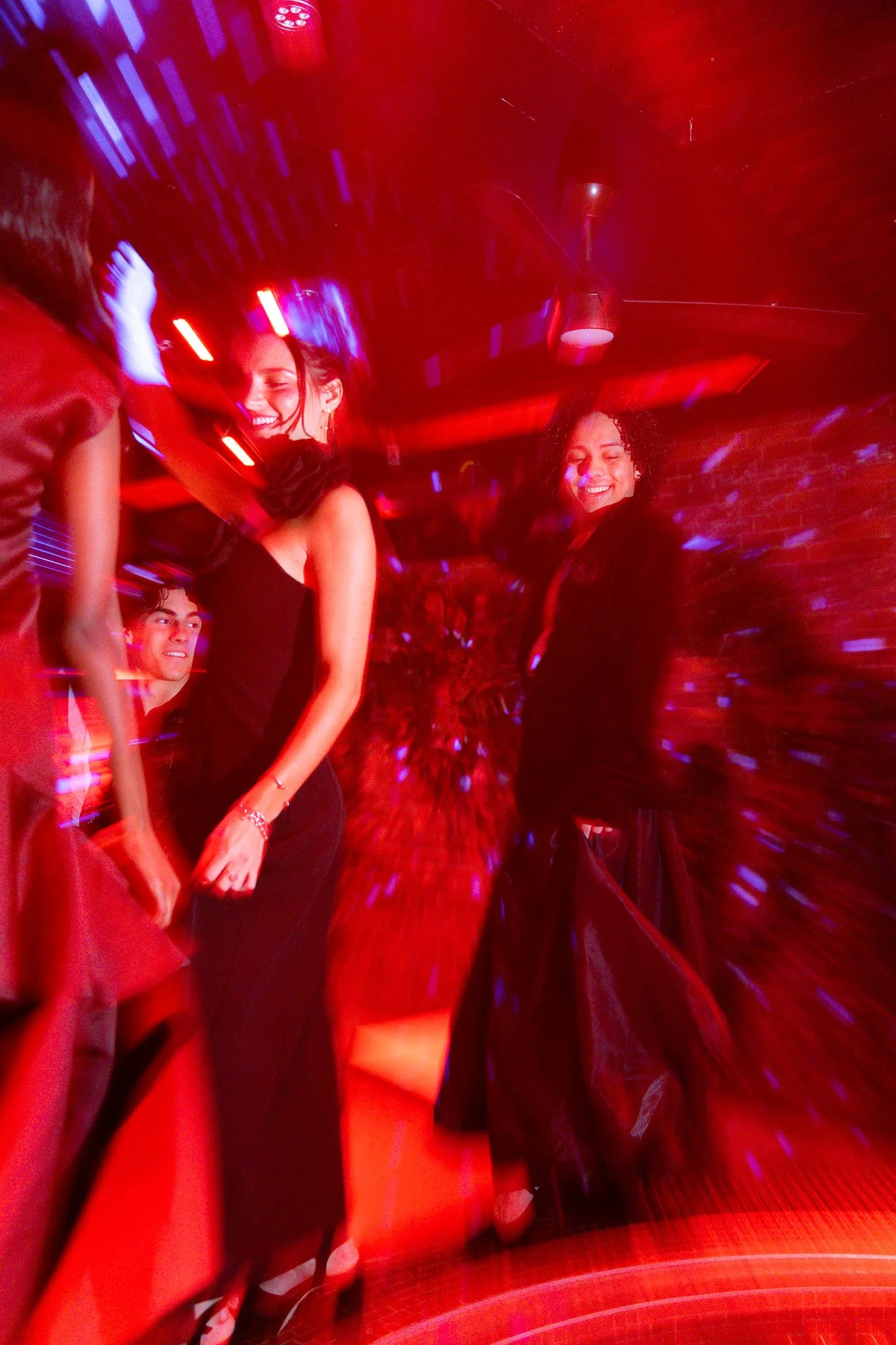 People dancing and smiling in a nightclub with red lighting and motion effects.