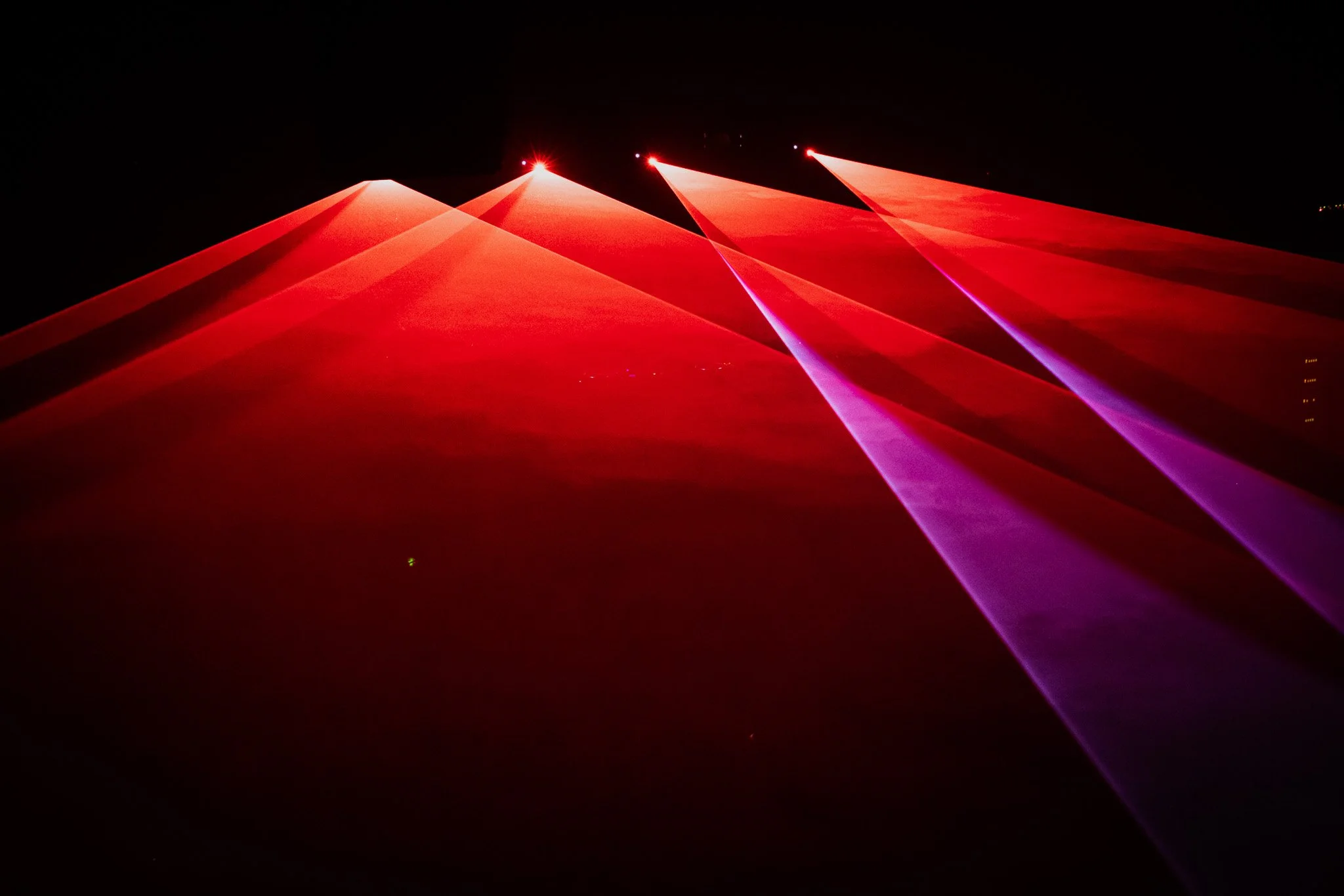 Colorful laser light beams projecting in the night sky, mainly in red and purple hues.