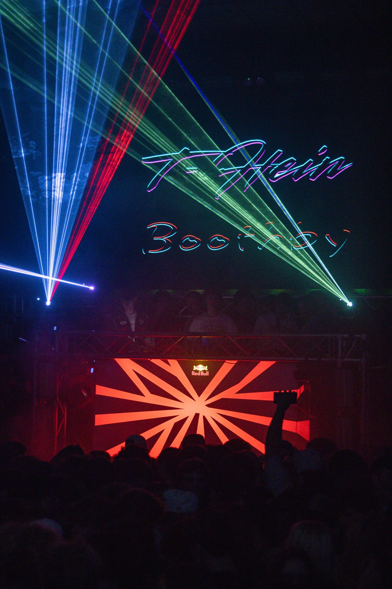 A concert scene with laser lights and a digital display reading 'Aven Bootey' above a crowd, with a DJ booth featuring a Red Bull logo.