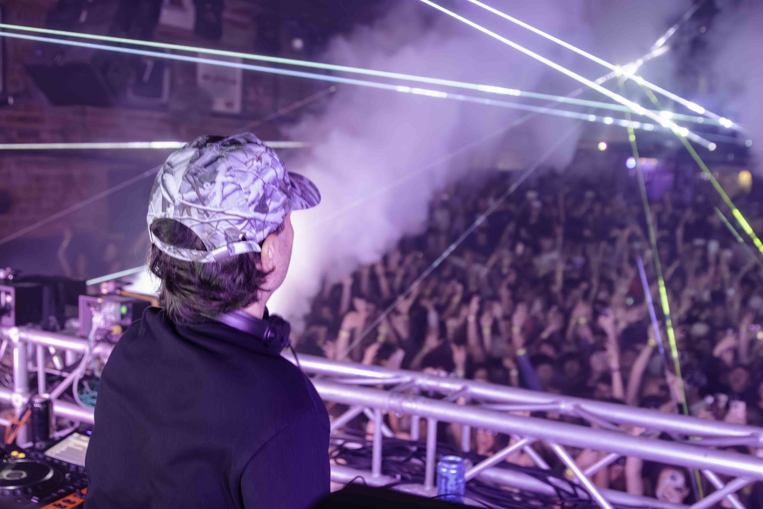 DJ performing at a nightclub or concert with a large crowd, colorful laser lights, and a smoky atmosphere.
