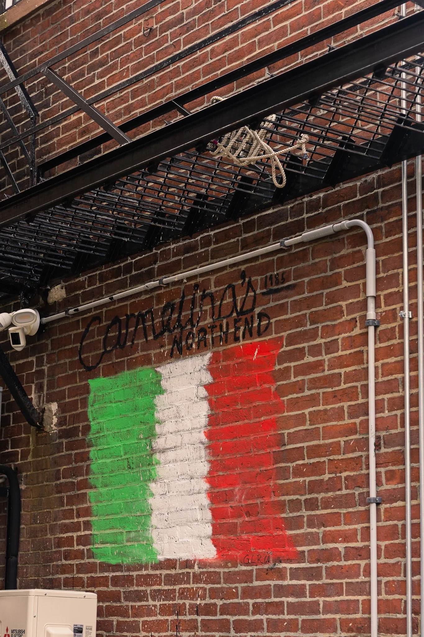 Graffiti of the Italian flag painted on a brick wall, with the text 'Cosa Nostra North End' written above, and 'Geria' written below.