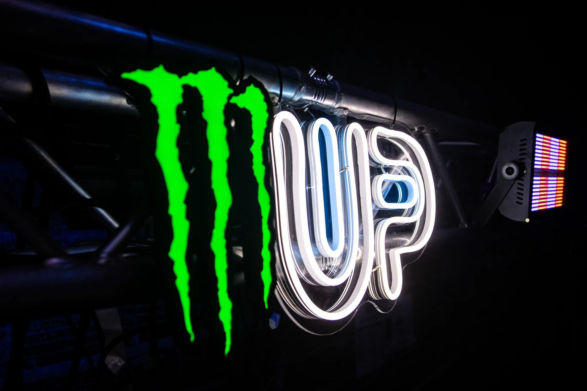Neon sign displaying the Monster Energy logo and the word 'UP' in some stylized text, with a dark background.