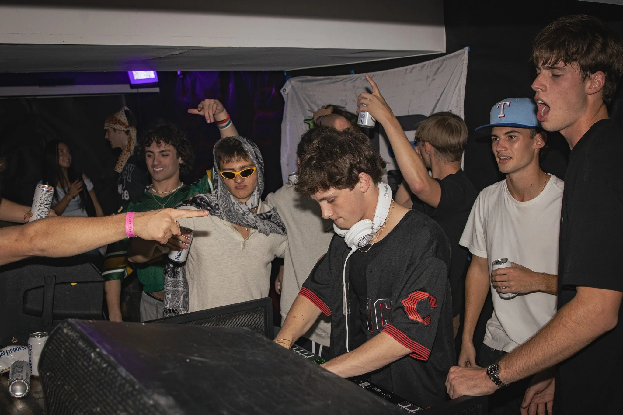 Group of young people at a DJ party, dancing and enjoying music, with one person DJing using a keyboard and wearing headphones.