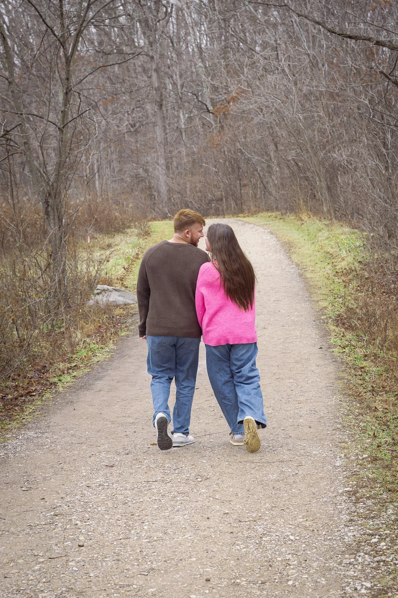 A couple walking together on a dirt path in a wooded area, holding hands and enjoying conversation.