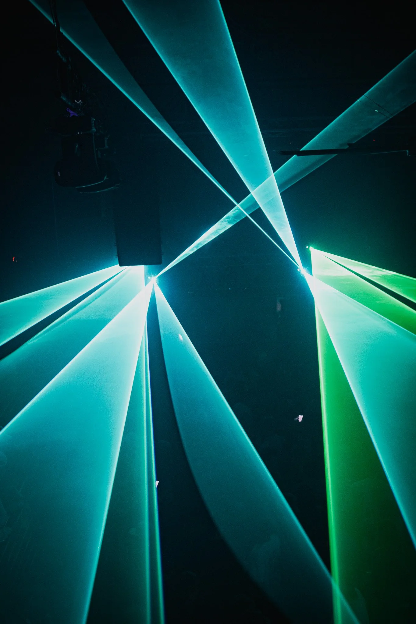 Colorful laser light beams projected in a dark space, creating intersecting lines of blue and green.
