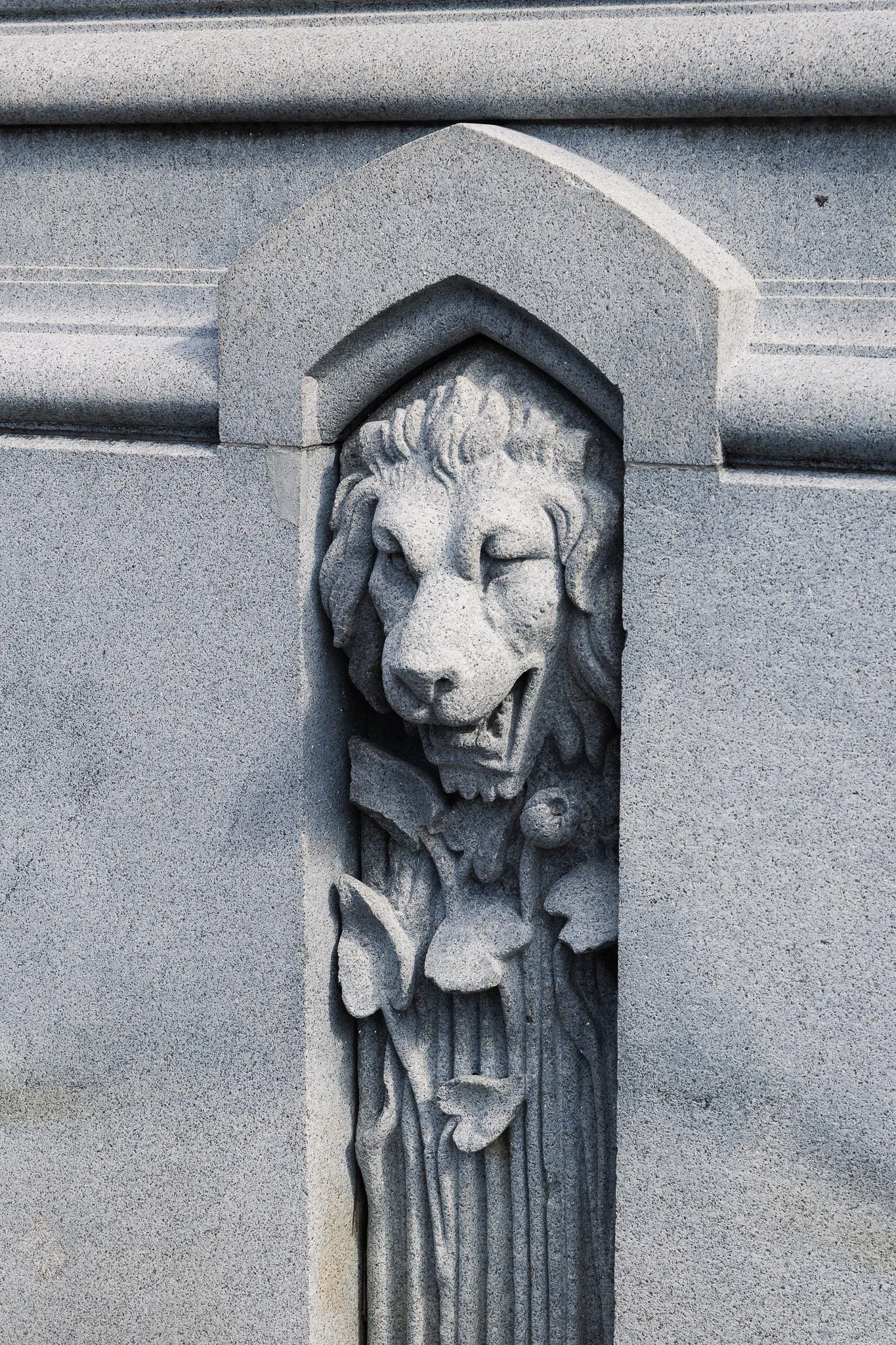 Stone sculpture of a lion's head carved into a building facade.