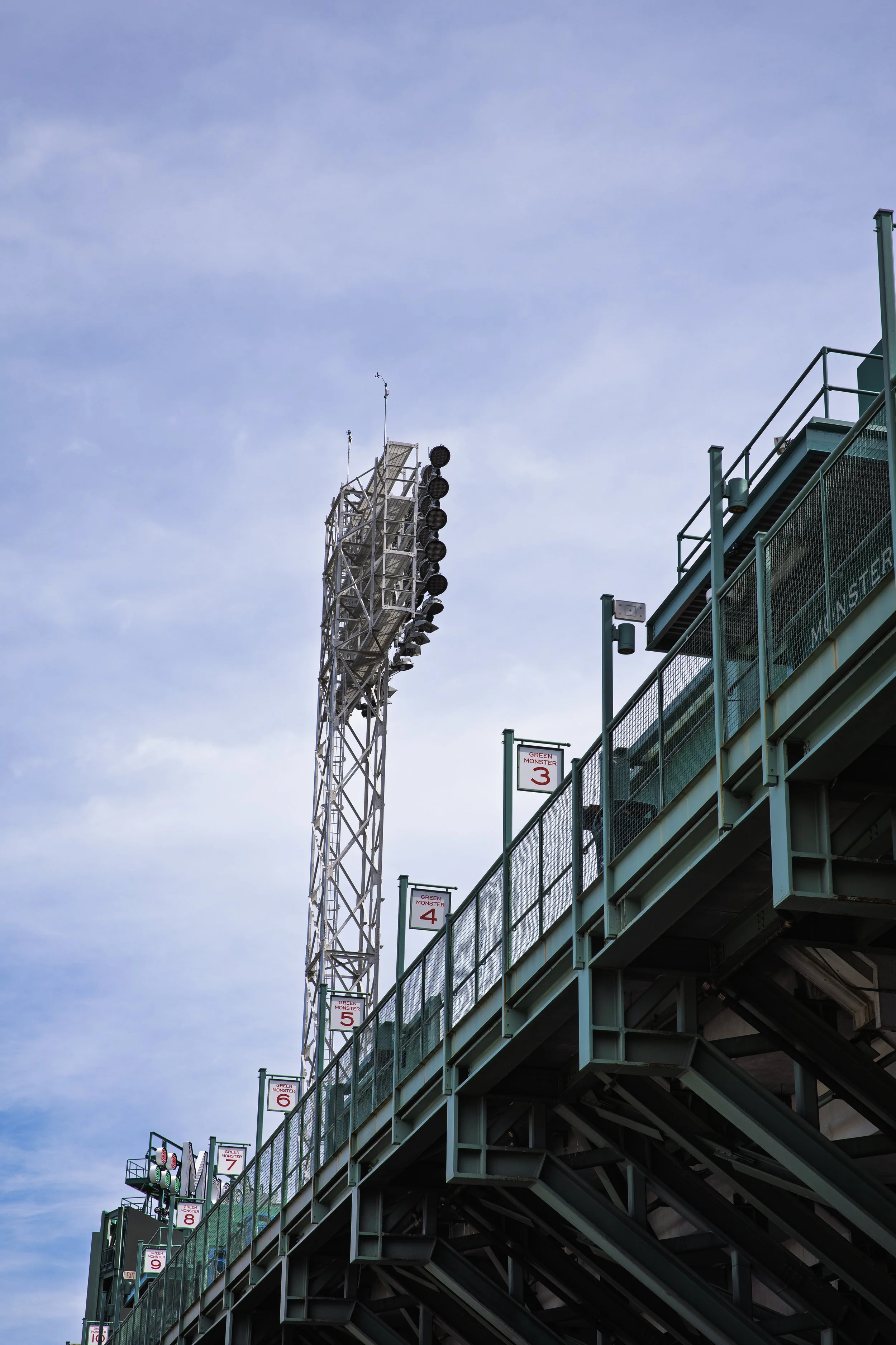 View of a Fenway Park baseball stadium seating area and light tower against a blue sky.