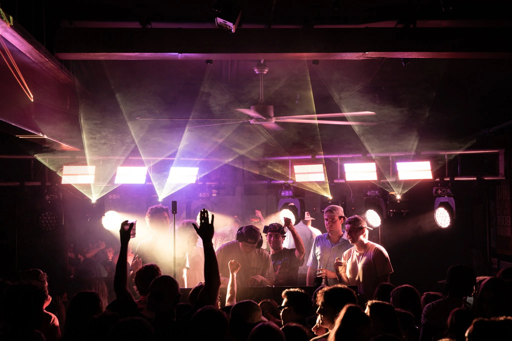 Crowd of people dancing at a concert with colorful lights and fog
