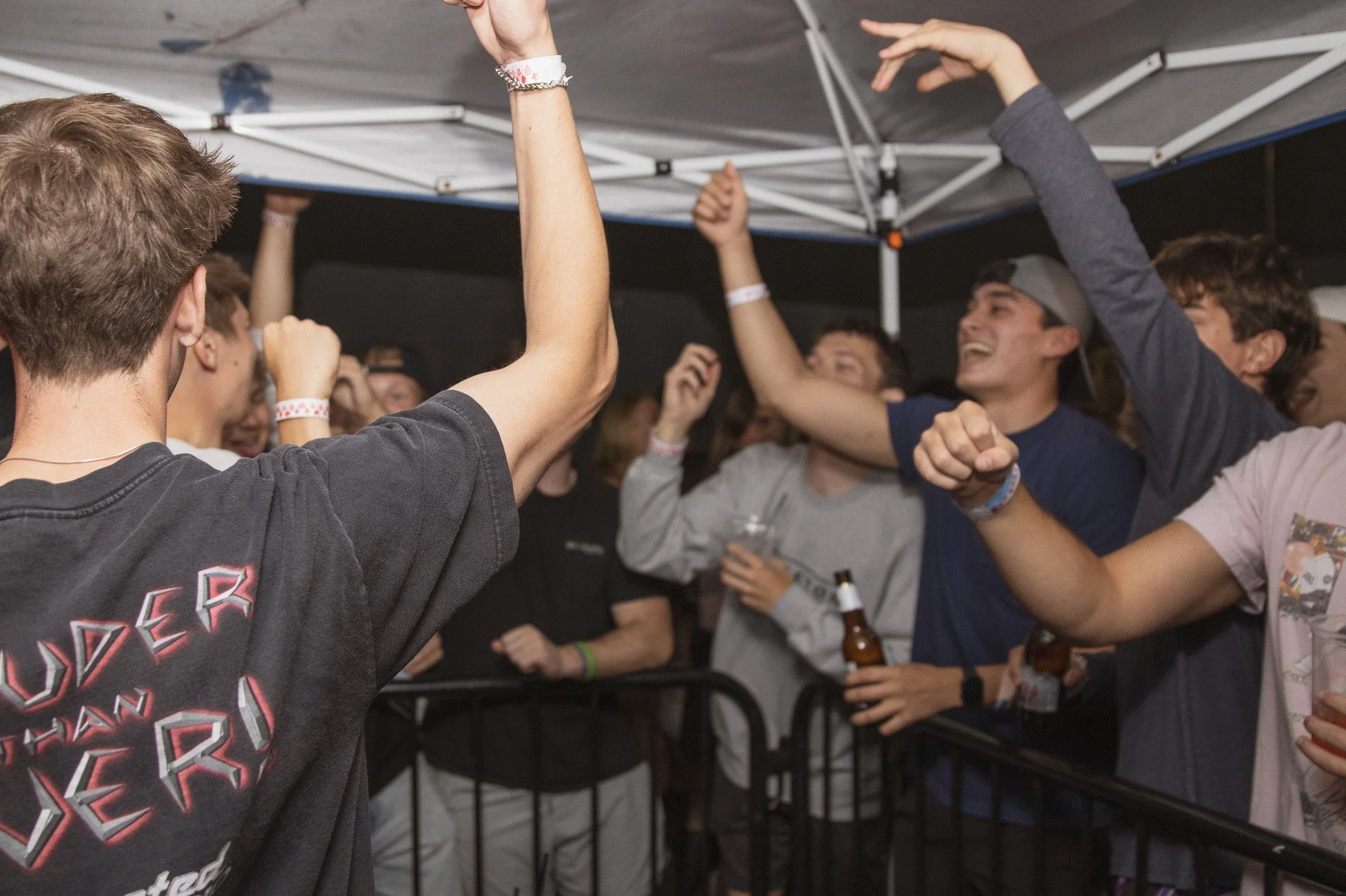 Group of young people at a party or concert, dancing and holding drinks, under a canopy.
