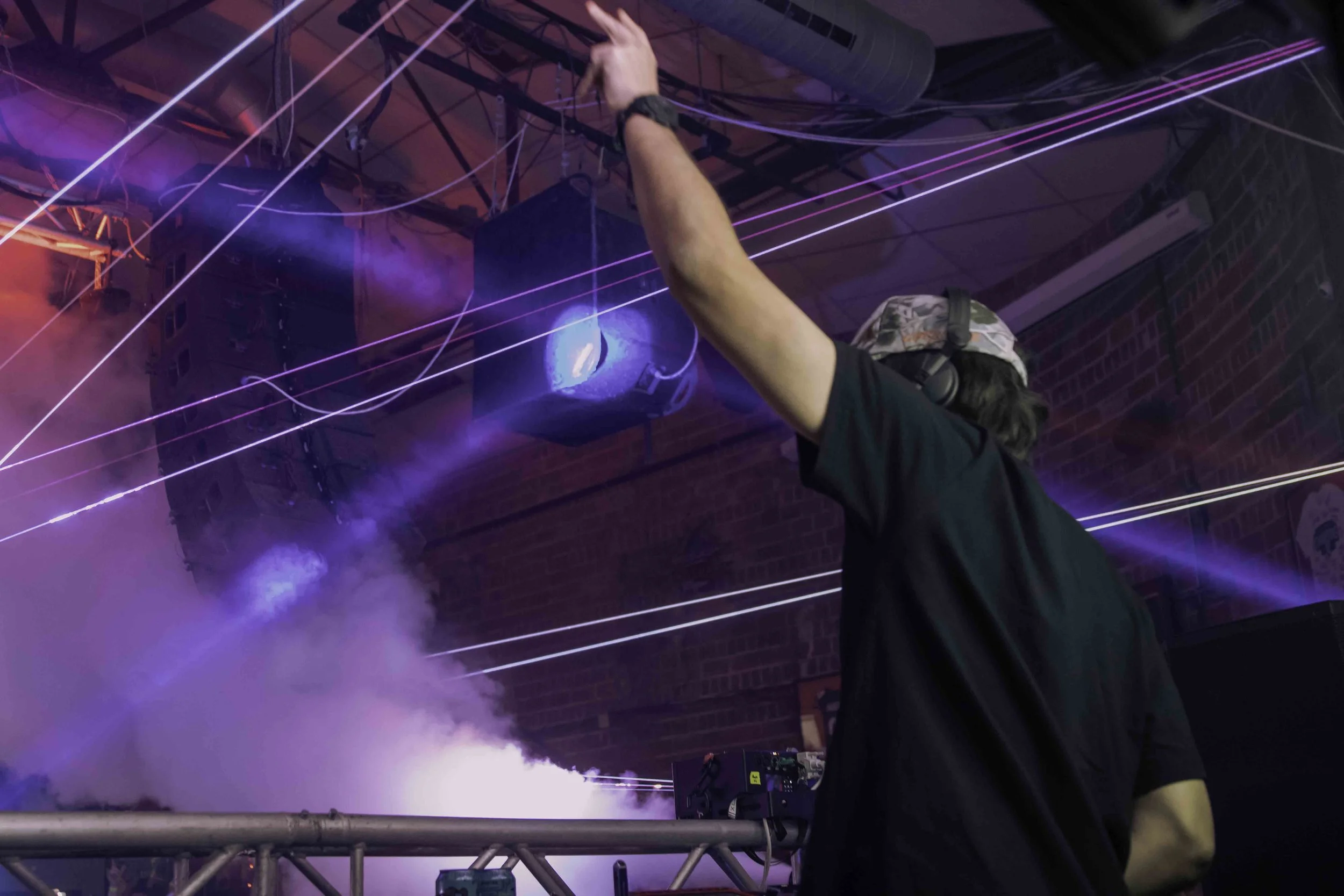 Person DJing at a nightclub with colorful laser lights and smoke effects.