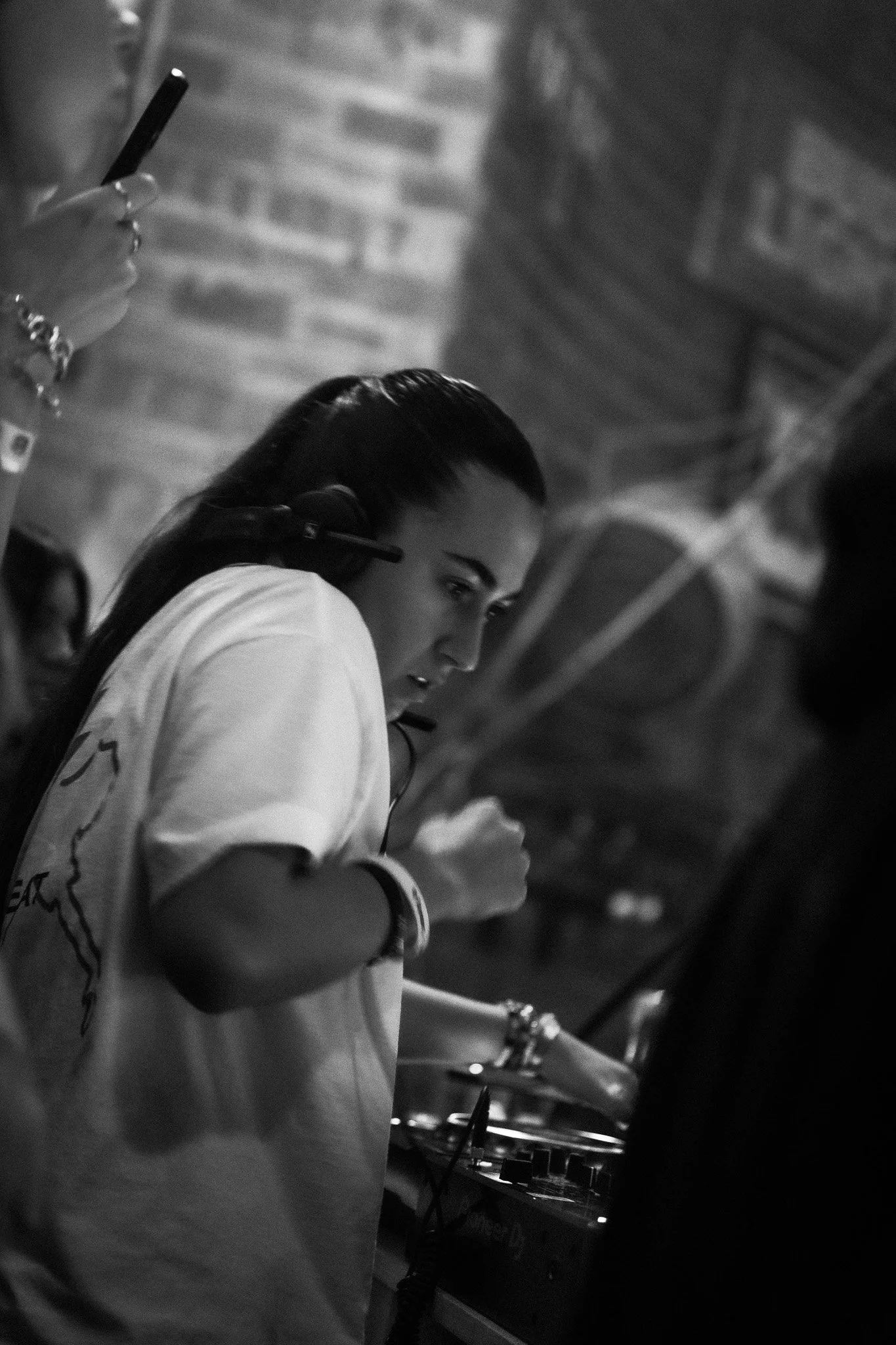 A woman wearing headphones, focused on DJ equipment, in a dimly lit indoor setting.