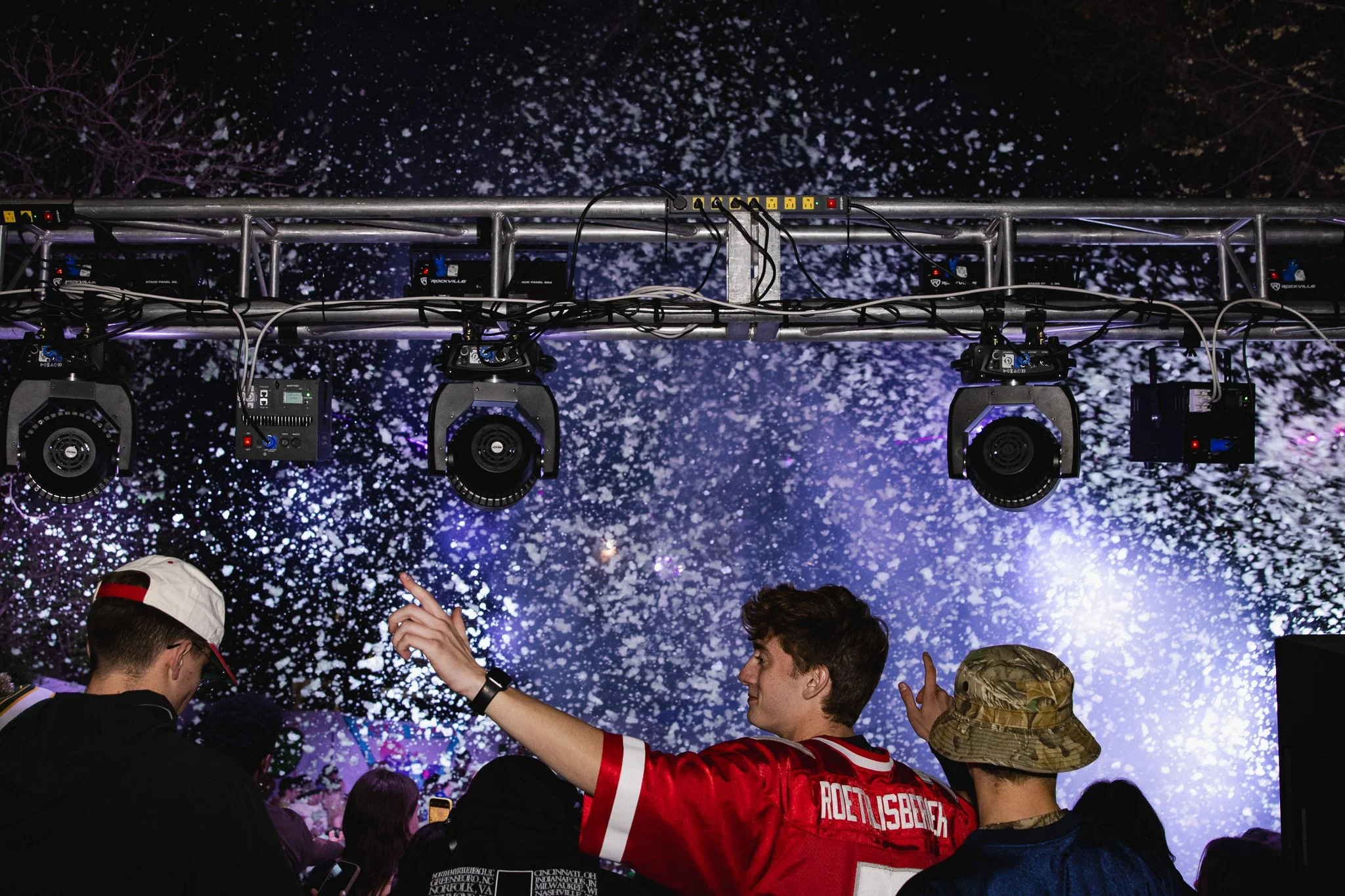 People at a concert or event with stage lights and confetti in the background.