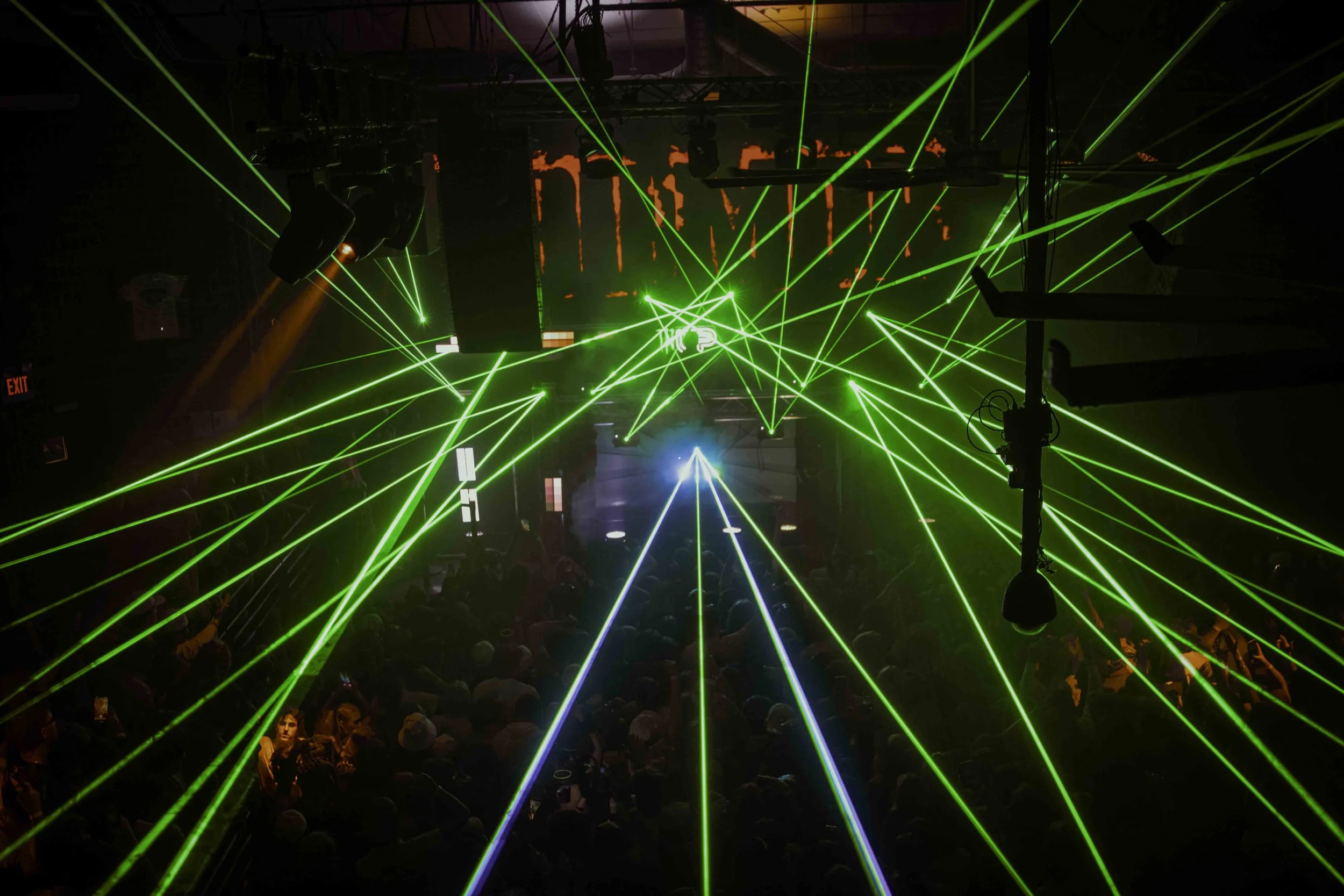 Dark nightclub scene with multiple green and blue laser beams crossing the space and a crowd of people dancing.