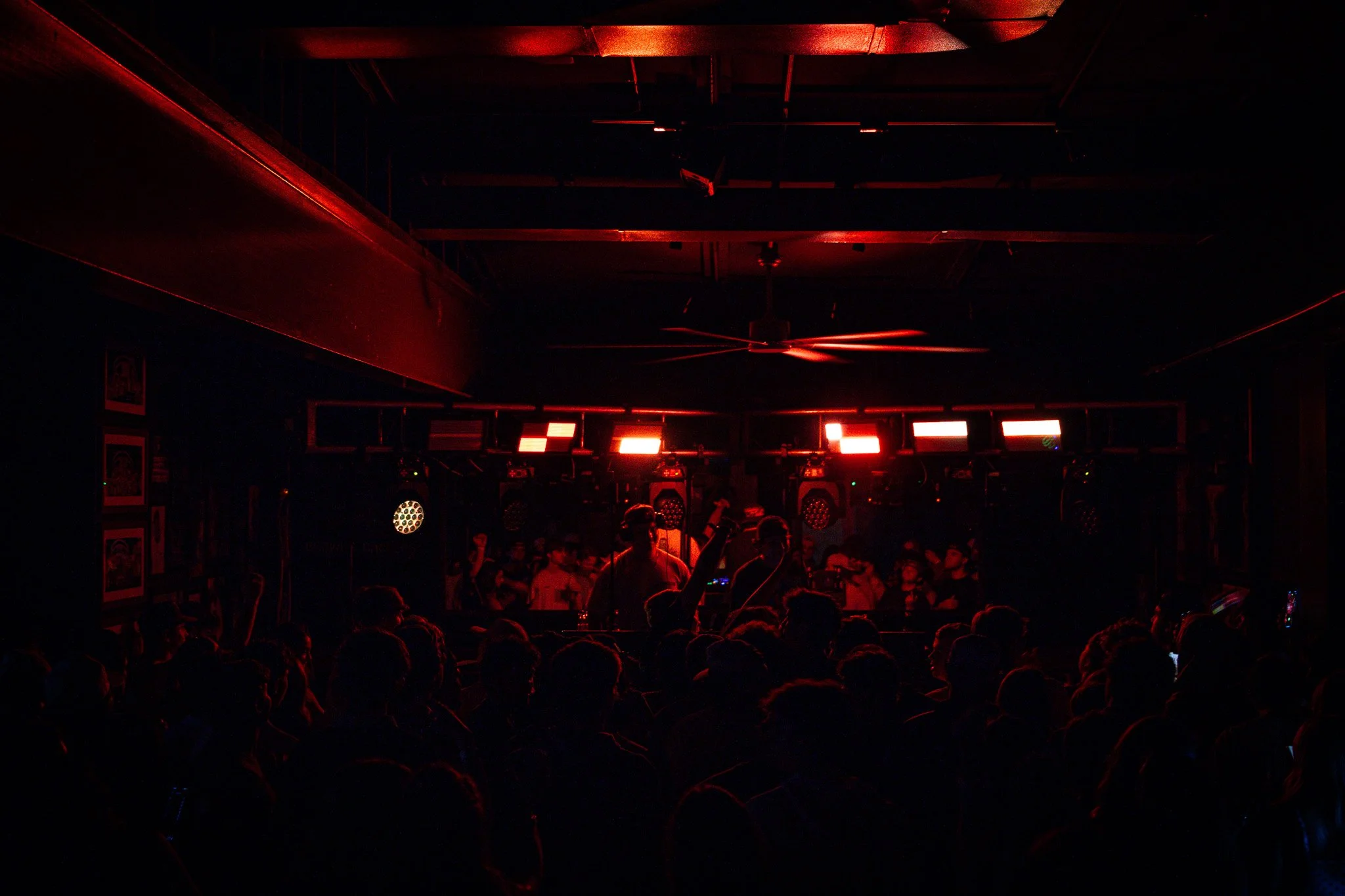 A dark nightclub with a DJ on stage, red lighting, and a crowd of people dancing and enjoying music.
