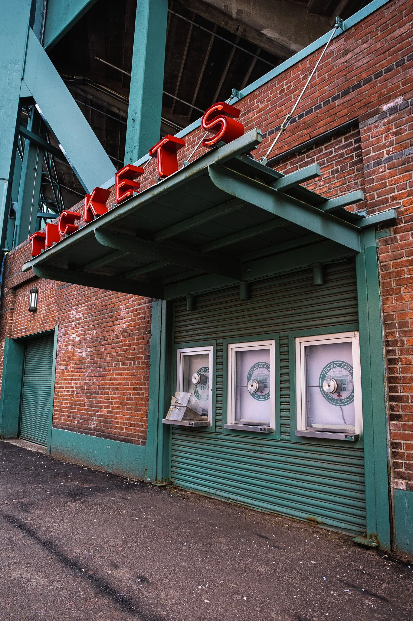 Photo of Fenway Park exit with red neon sign on green metal awning, brick wall, ticket booths, and exit door