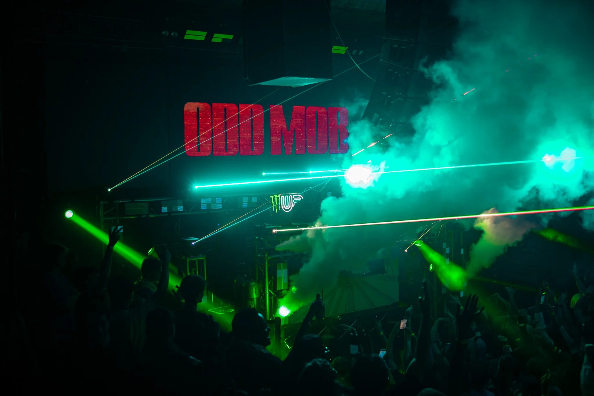 Concert scene with green laser lights, smoke, crowd raising hands, and a large screen displaying red text 'ODD MOB'.