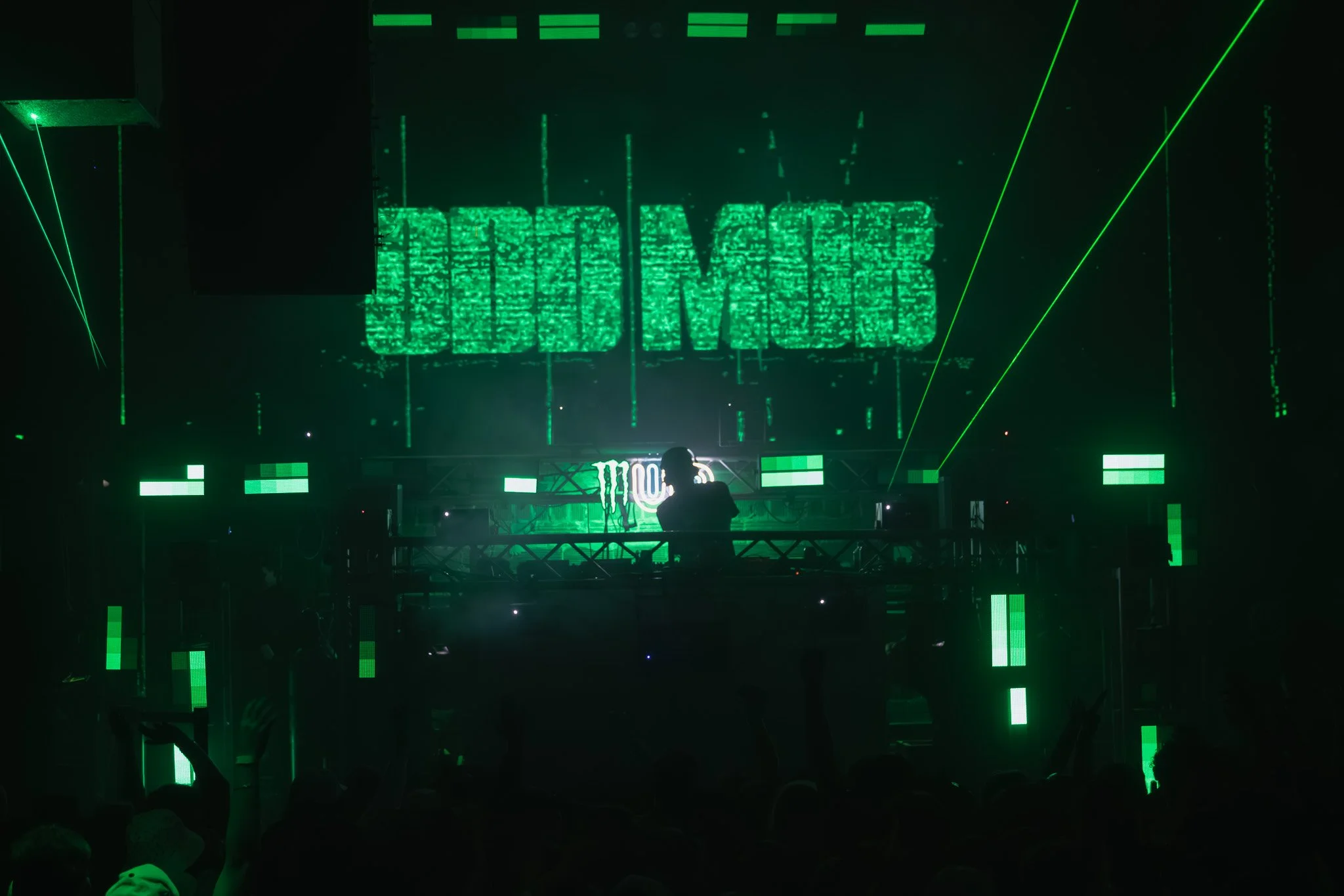A DJ performing at a nightclub with green laser lights and a large screen displaying the text 'EDM CLUB' in bright green.