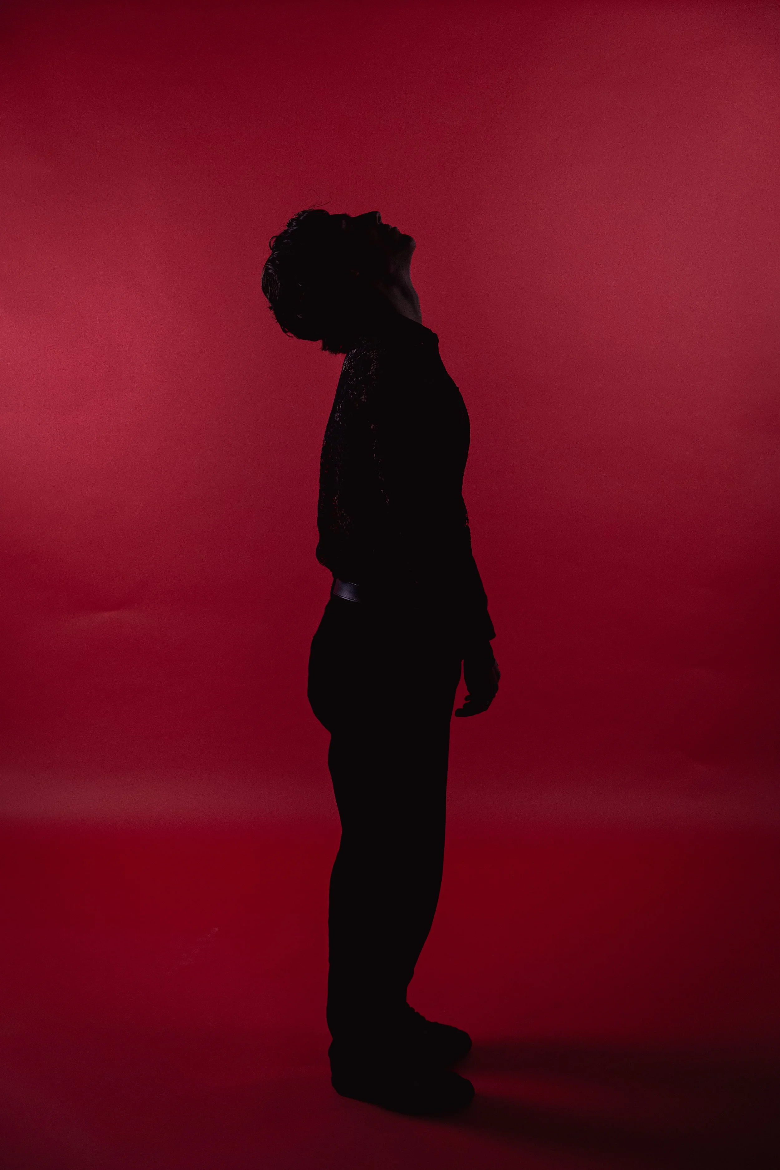 Silhouette of a person standing with head tilted back, against a red gradient background.