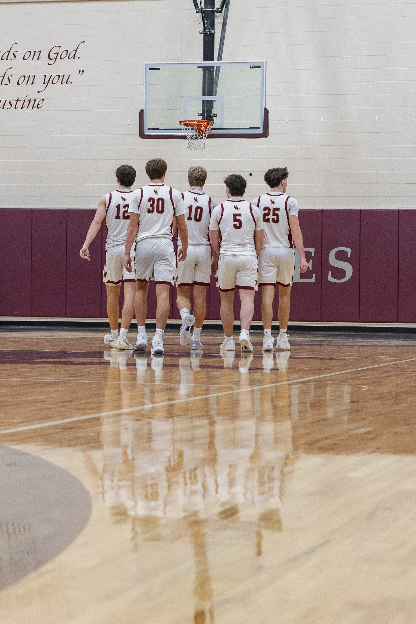 Six basketball players in white uniforms walking towards the basket on a wooden court.