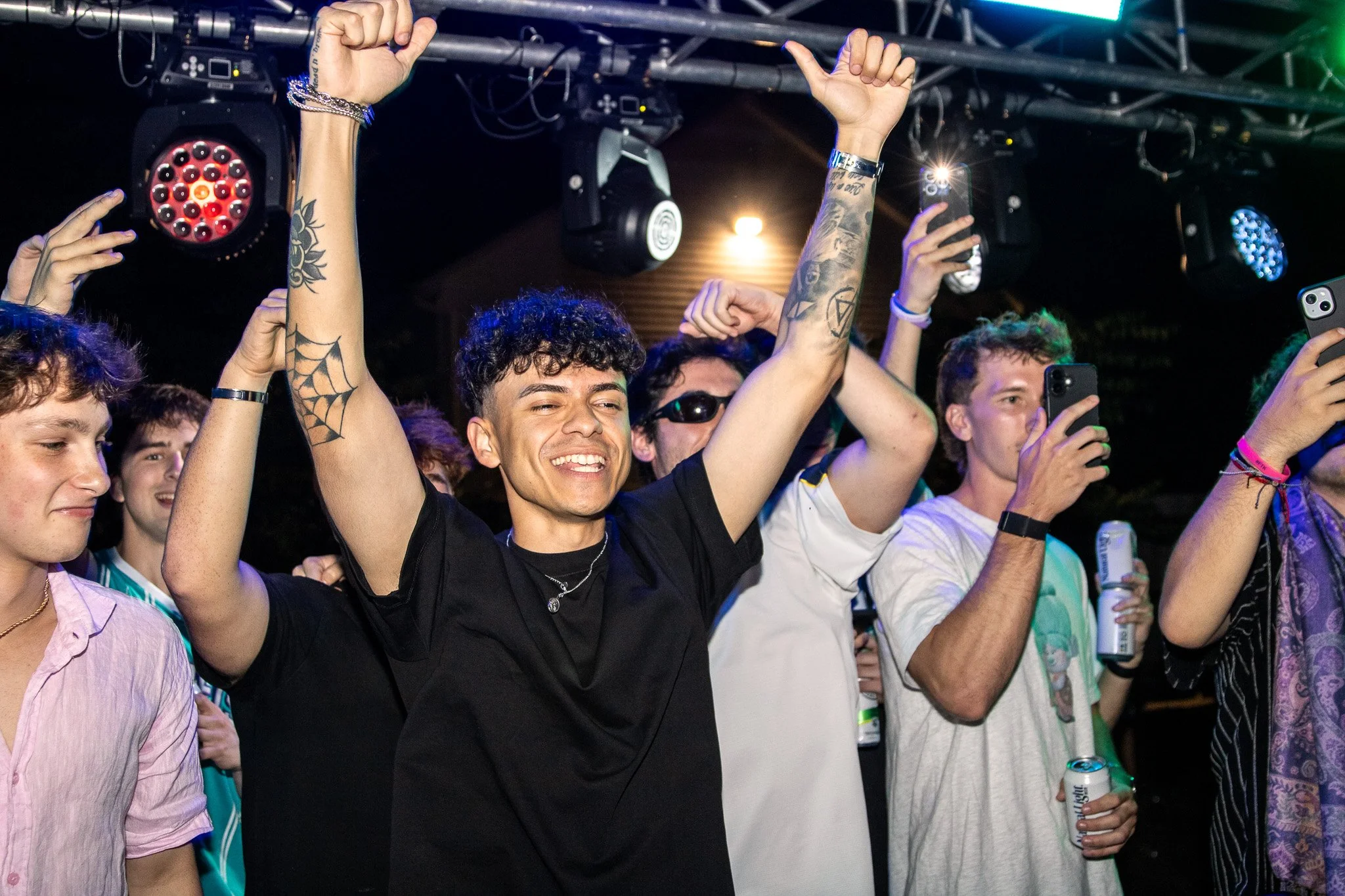 A group of young people enjoying a concert, with one person in the center raising their hands and smiling.