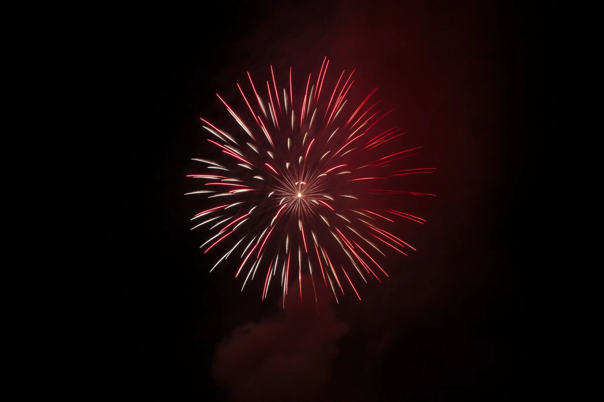 A bright firework exploding in the night sky with red and white streaks radiating outward from the center.