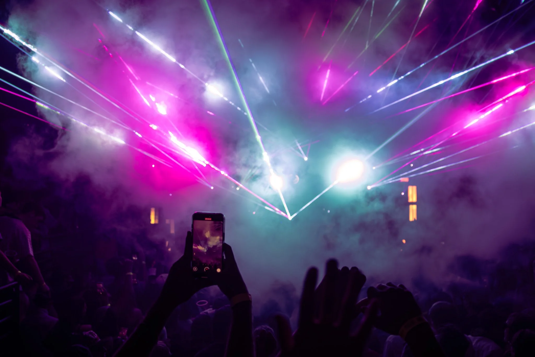 A concert with laser lights and smoke effects, audience members capturing the moment on smartphones.