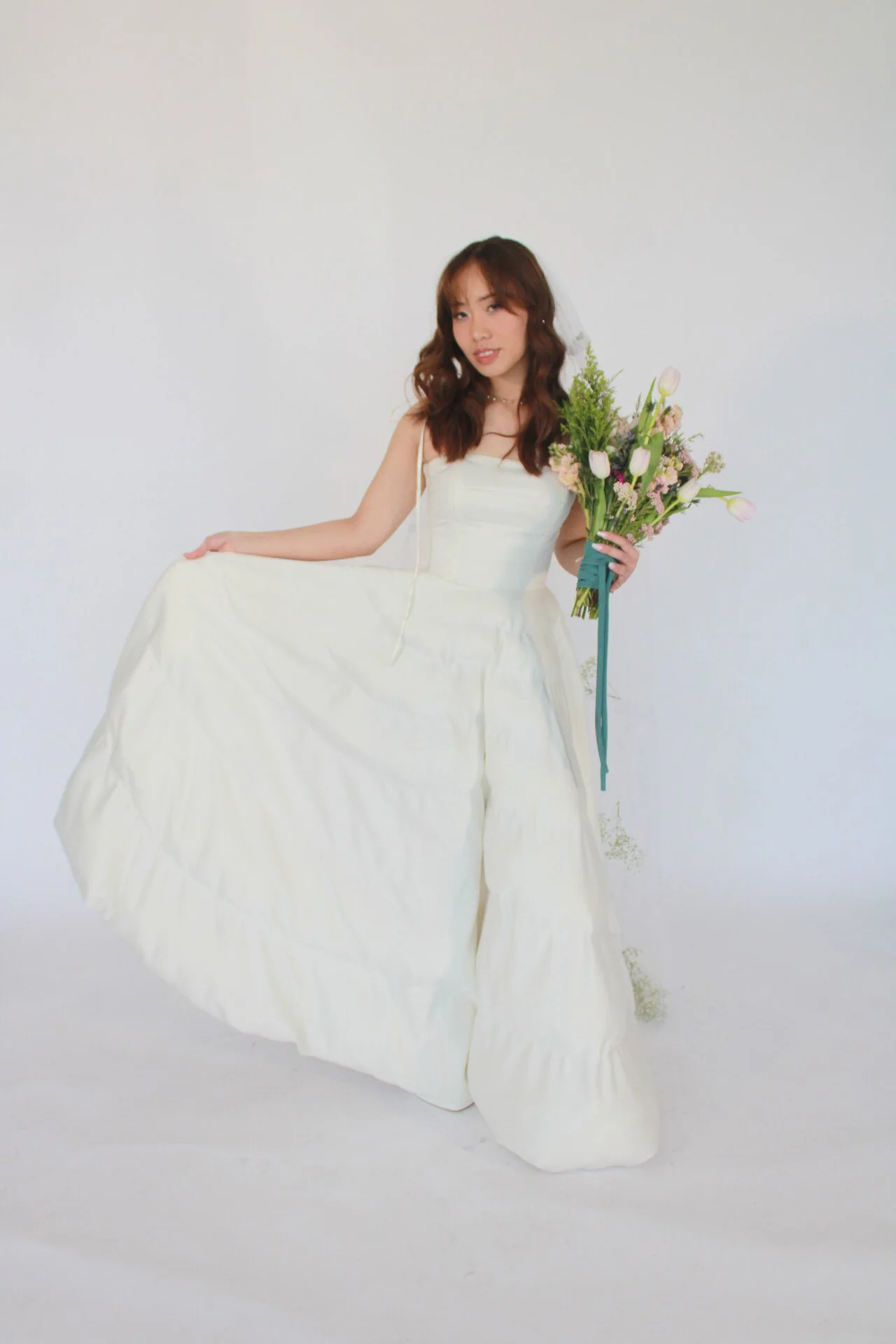 A woman in a white dress holding a bouquet of flowers against a plain white background.