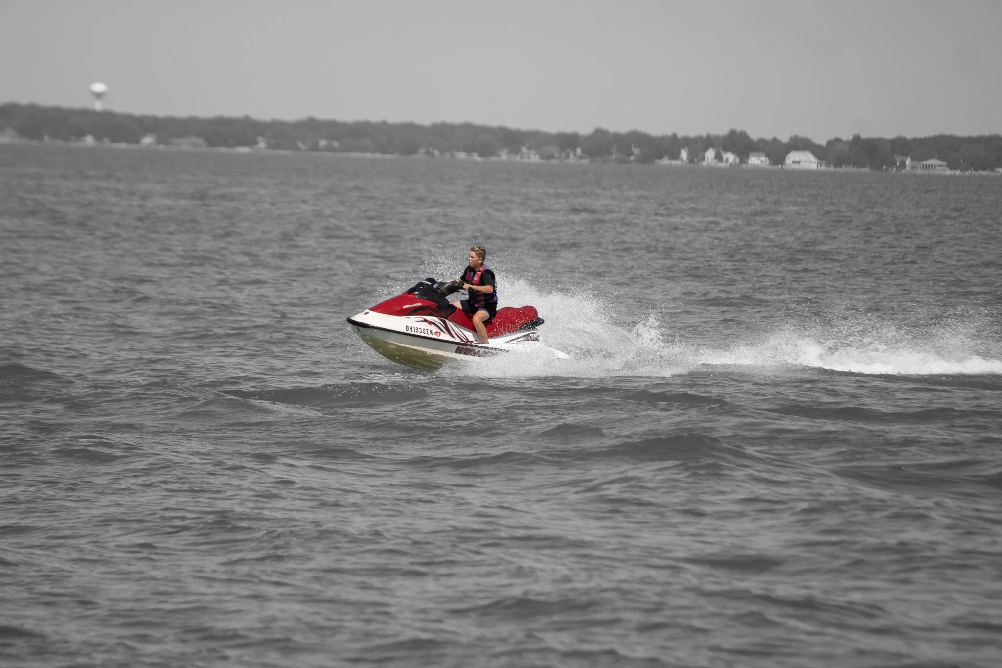 A person riding a red and white jet ski on a body of water, with a distant shoreline in the background.