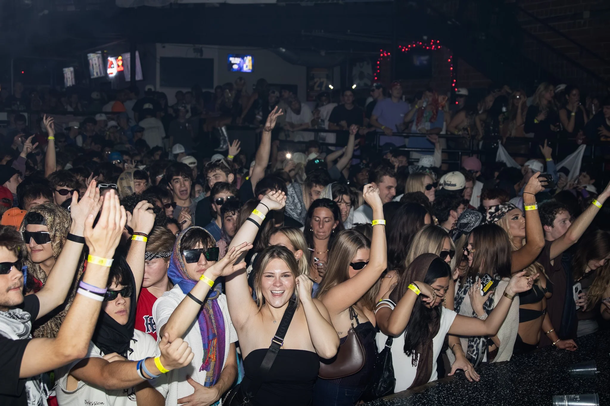 Crowd of people dancing and enjoying a concert or music event in a dark indoor venue.