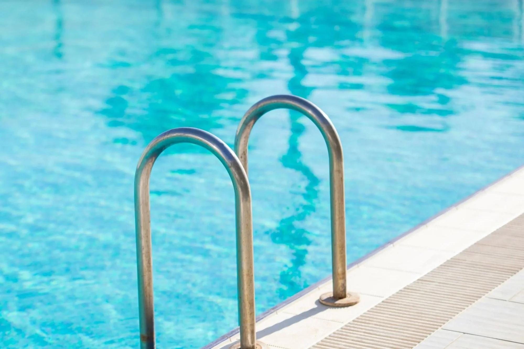 Close-up of metal pool ladder against the blue water of a swimming pool.