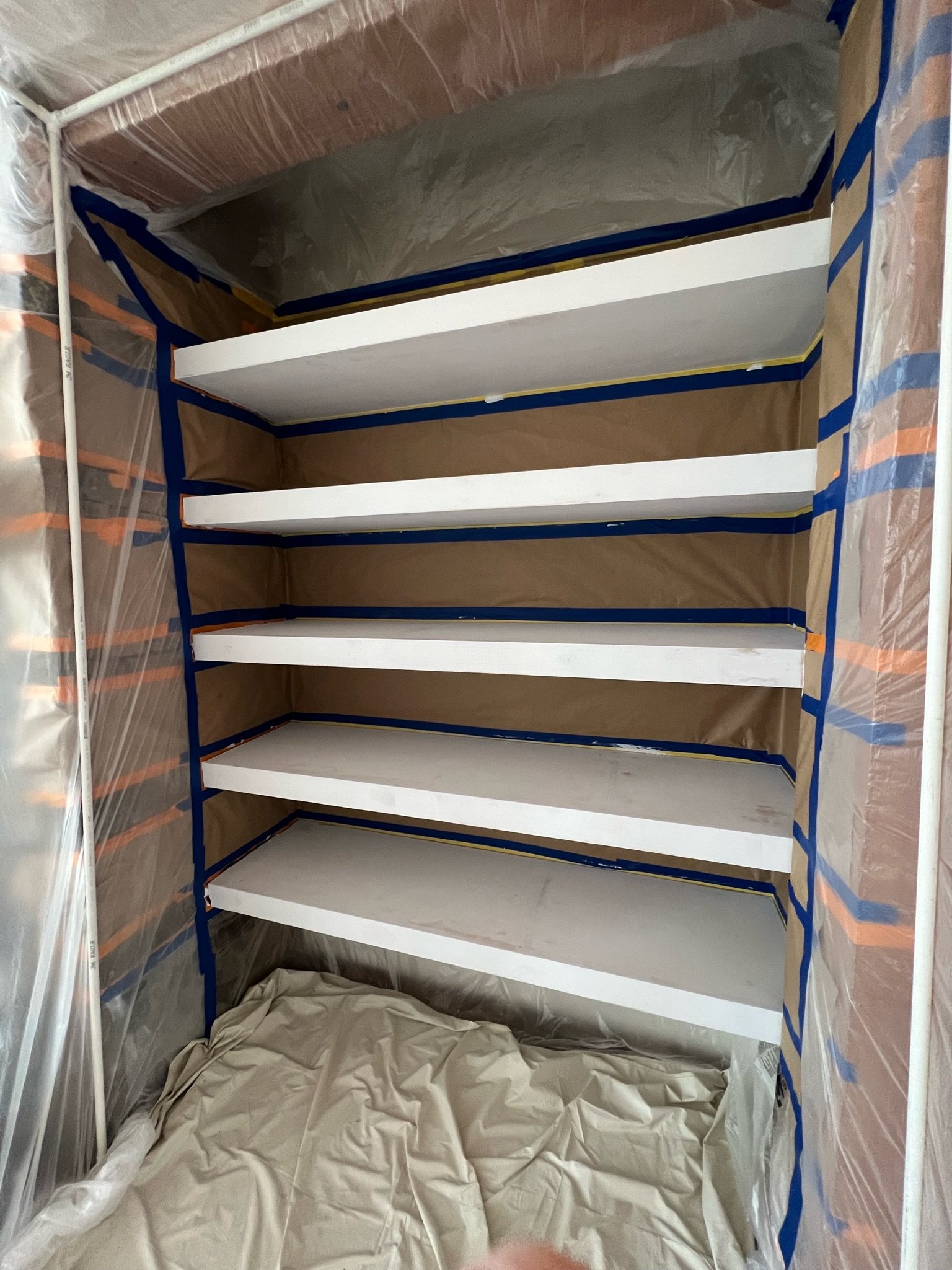 Painted white shelving unit with protective tape and plastic sheets for a painting project in progress.