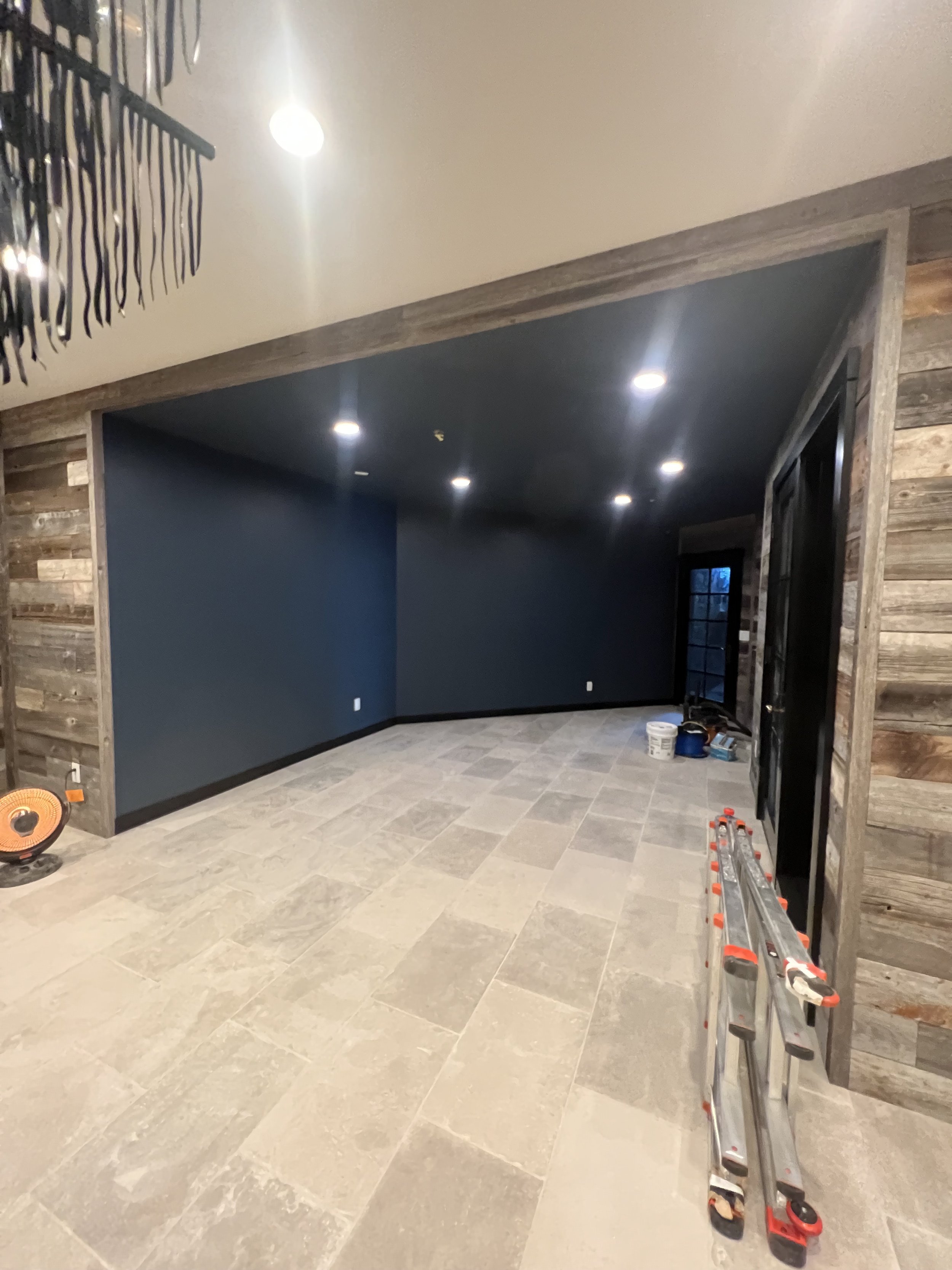 Interior room under renovation with dark walls, recessed lighting, gray tiled floor, a ladder, and a space heater.