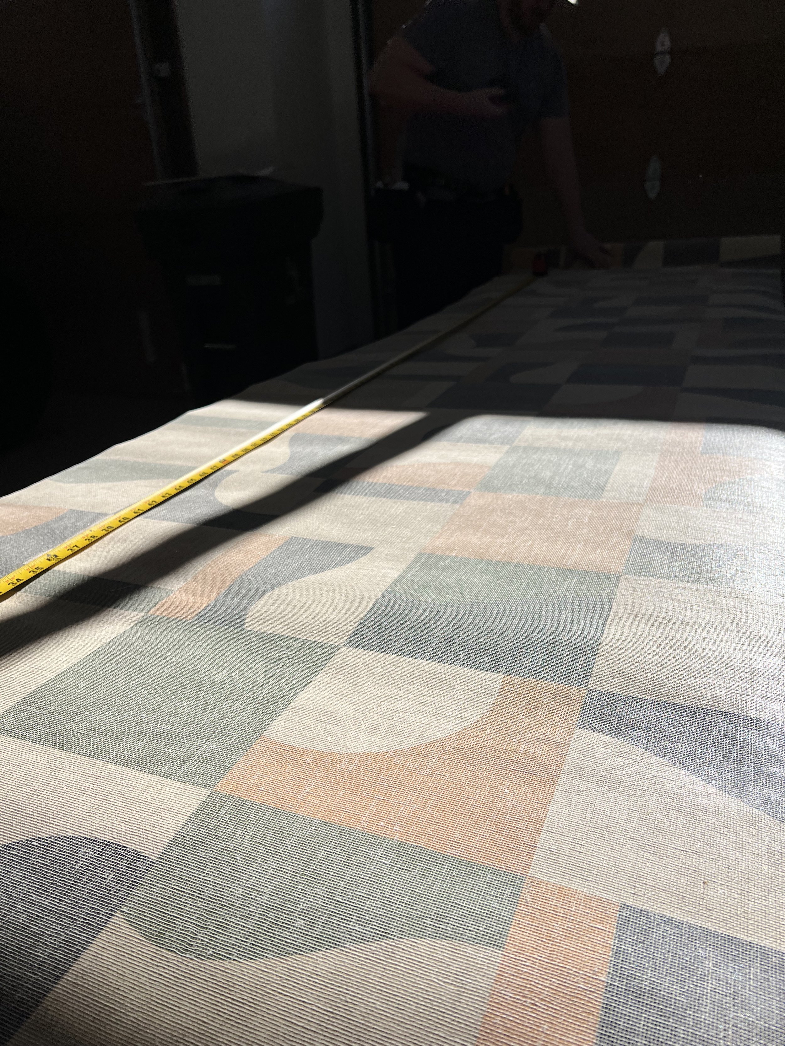 Person measuring fabric on a patterned textile surface with a measuring tape in a dimly lit room.