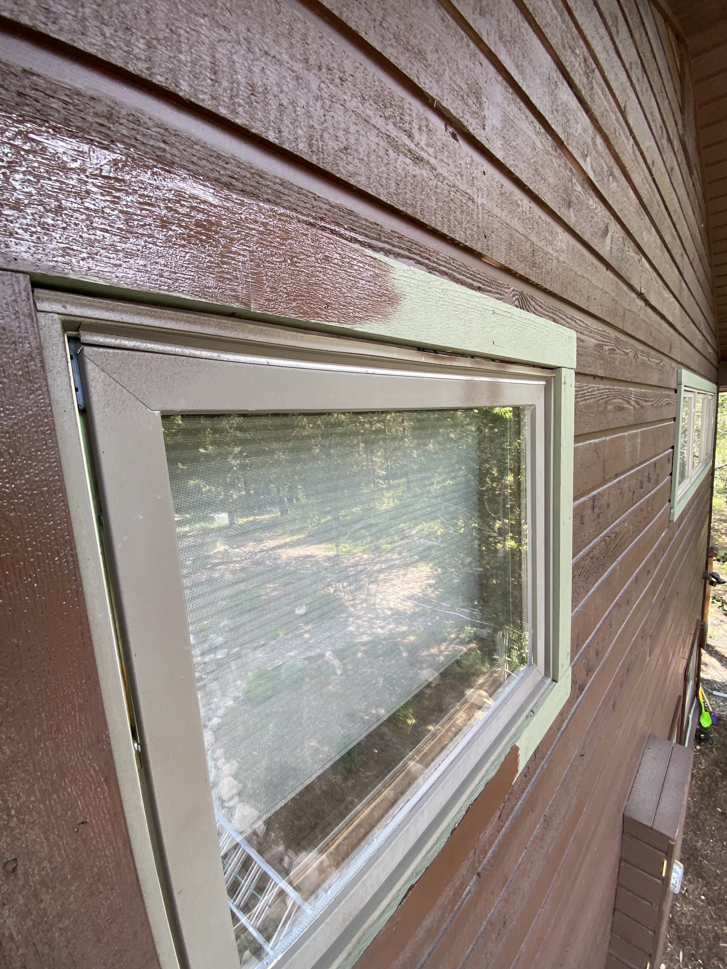 Close-up of a brown wooden wall with a window, showing mismatched paint areas.