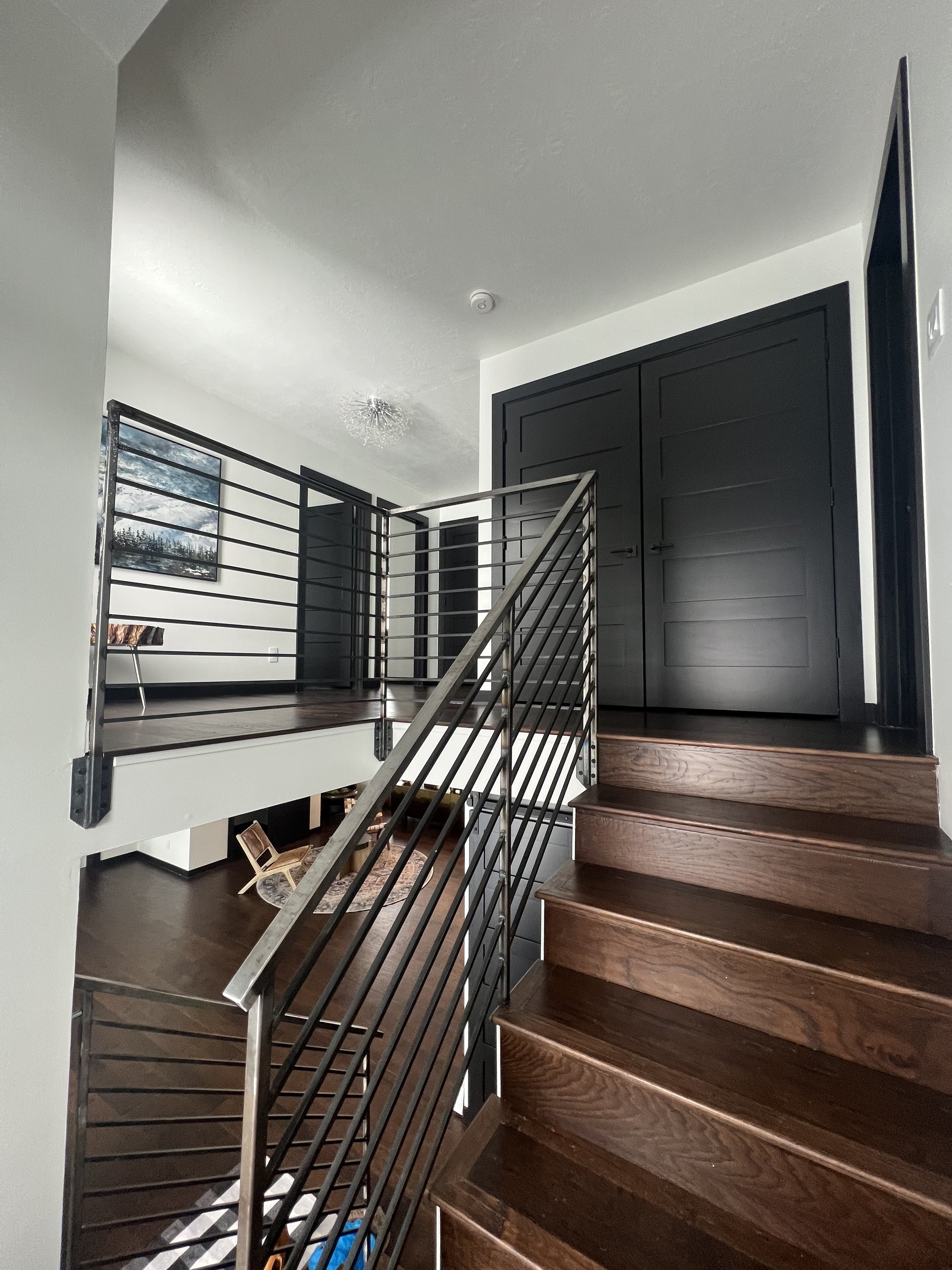 Modern interior with wooden stairs, metal railing, dark doors, and artwork on light walls