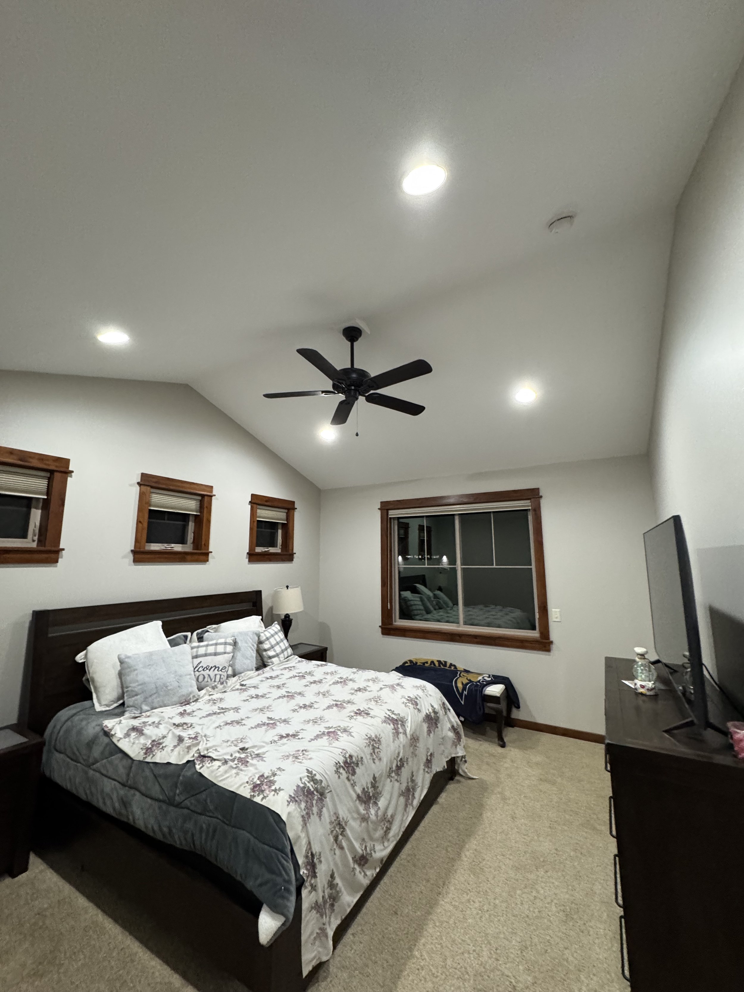 Bedroom with a bed, floral bedding, pillows, nightstands, ceiling fan, recessed lights, and a TV on a dresser.