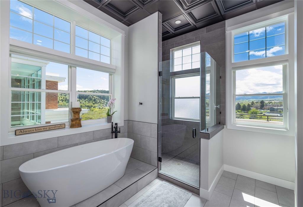 Modern bathroom with a freestanding bathtub, glass shower, and large windows with scenic views.