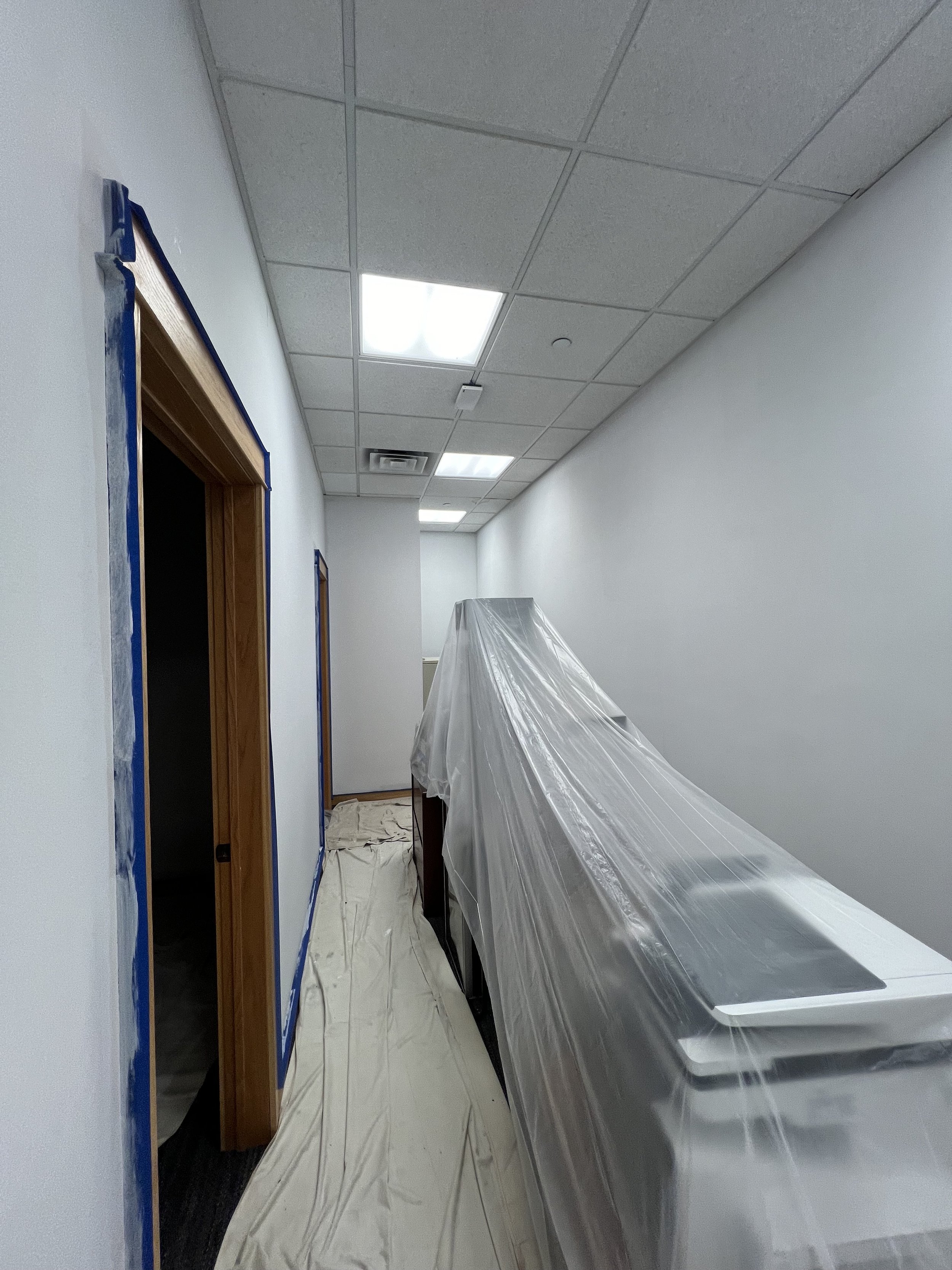 Hallway under renovation with plastic covered furniture and drop cloths on floor.