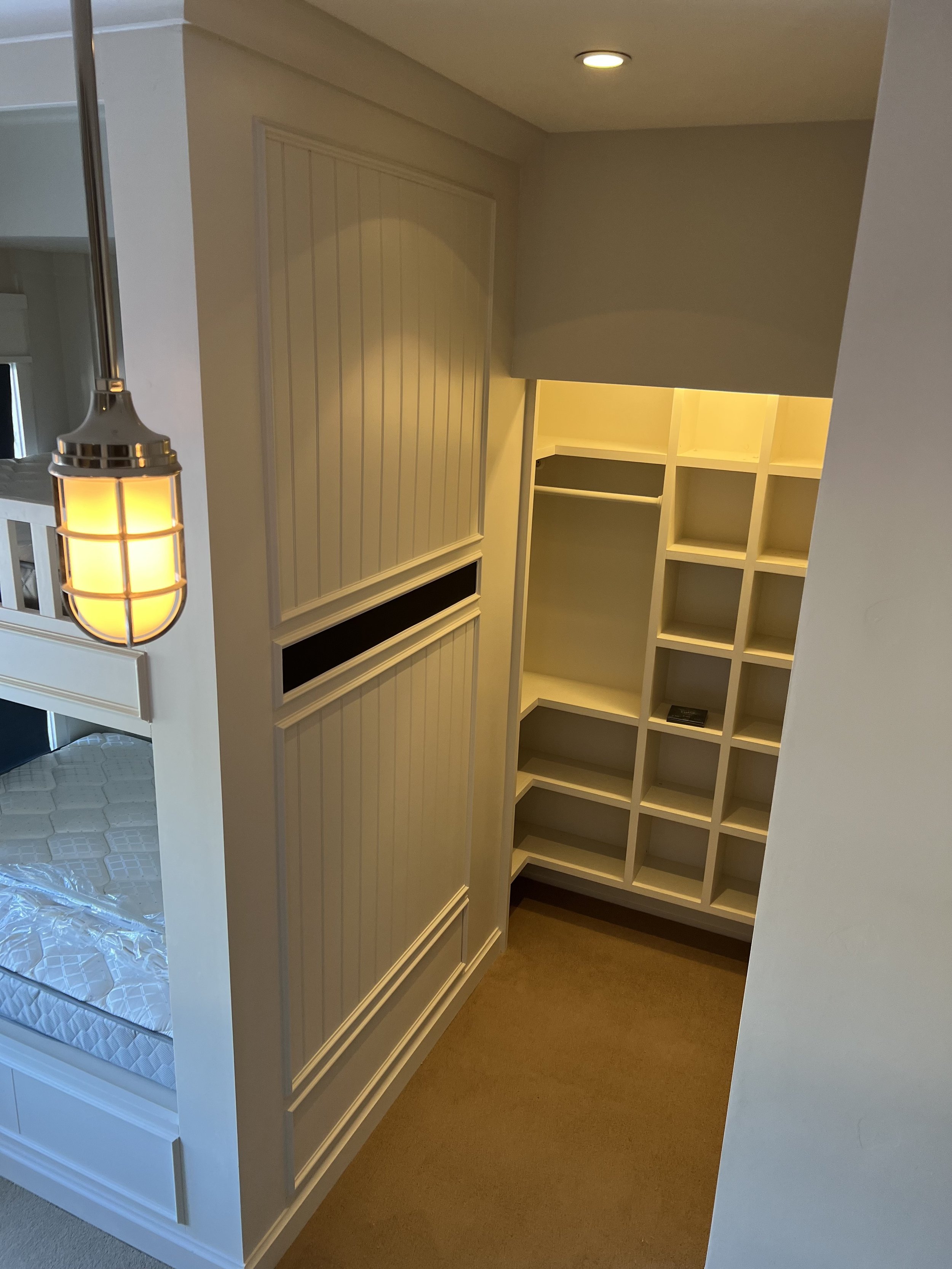 Interior view of a minimalistic white shelving unit and bunk bed, with a pendant light hanging from the ceiling.