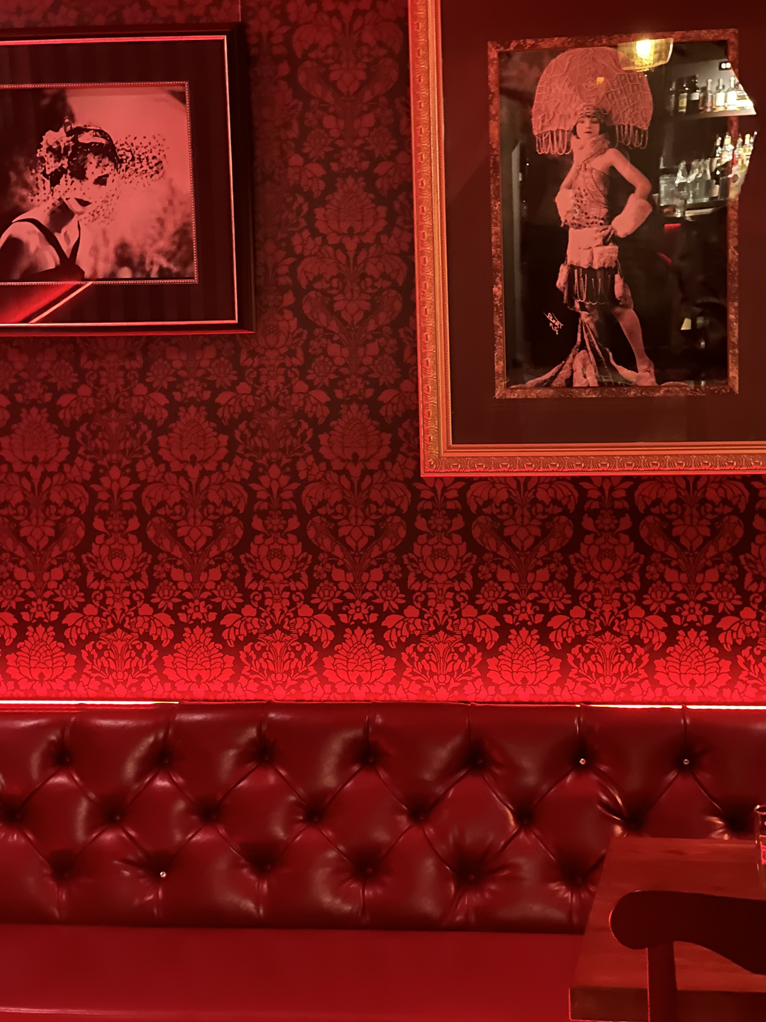Vintage-themed interior with red wallpaper, framed photographs, and a leather sofa.