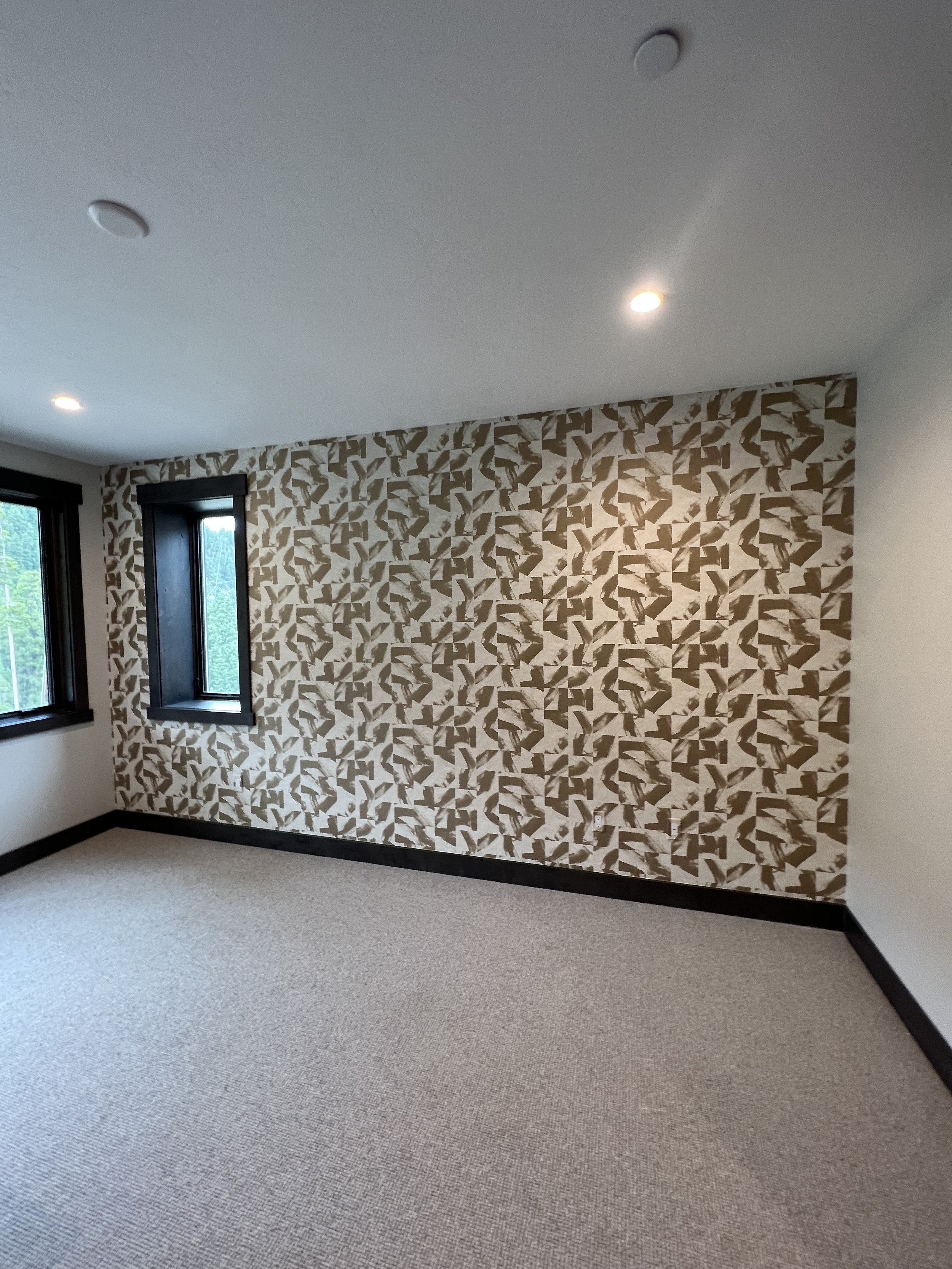 Empty room with patterned wallpaper, beige carpet, two windows, and recessed lighting.