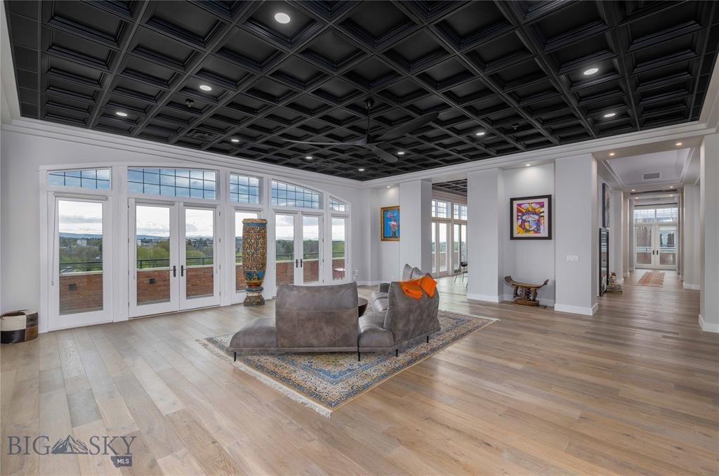 Modern living room with large windows, black coffered ceiling, light wood flooring, gray sofa, colorful artwork, and a decorative vase.