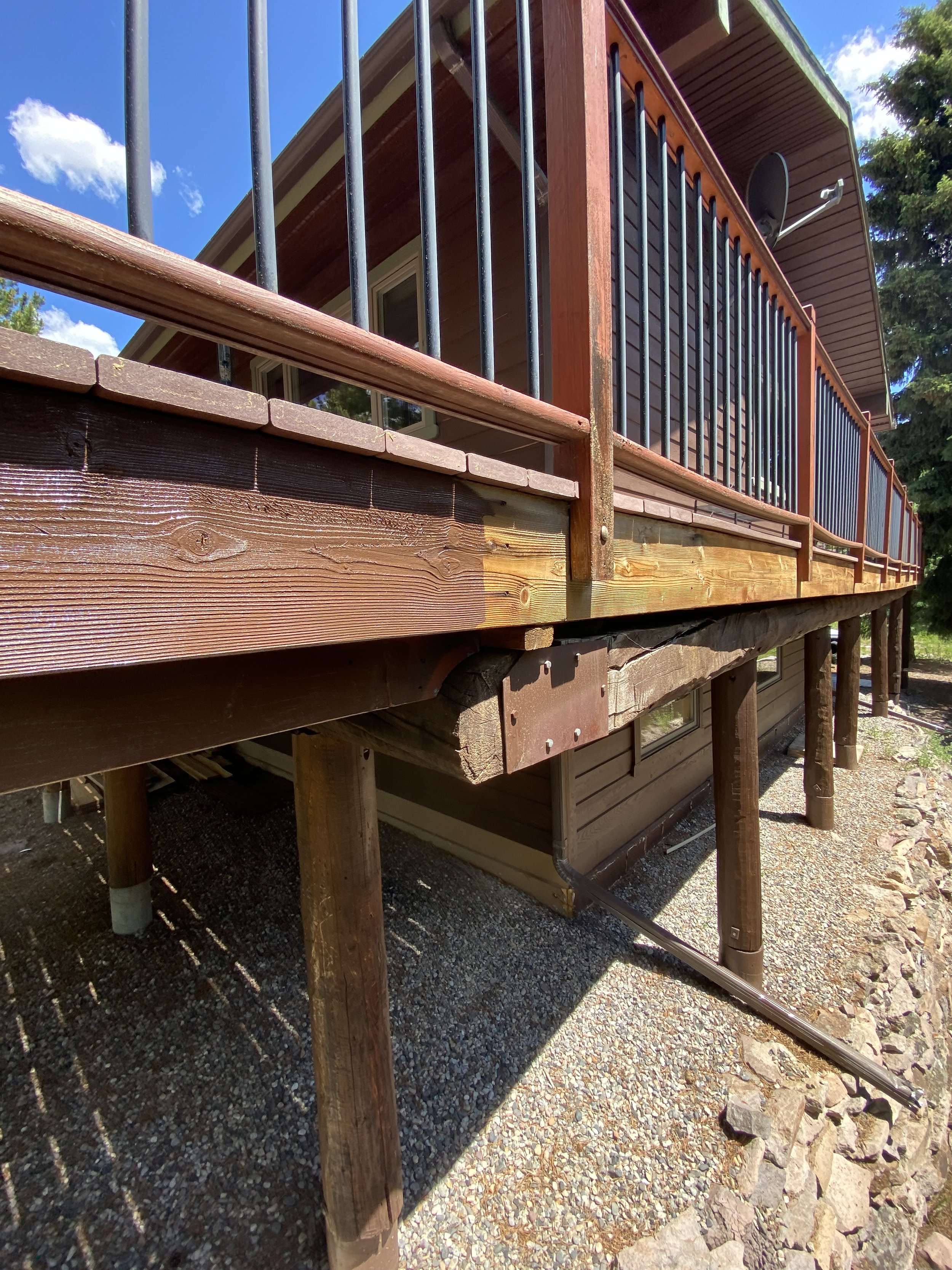 Elevated wooden deck with metal railings and gravel underneath, attached to a house.