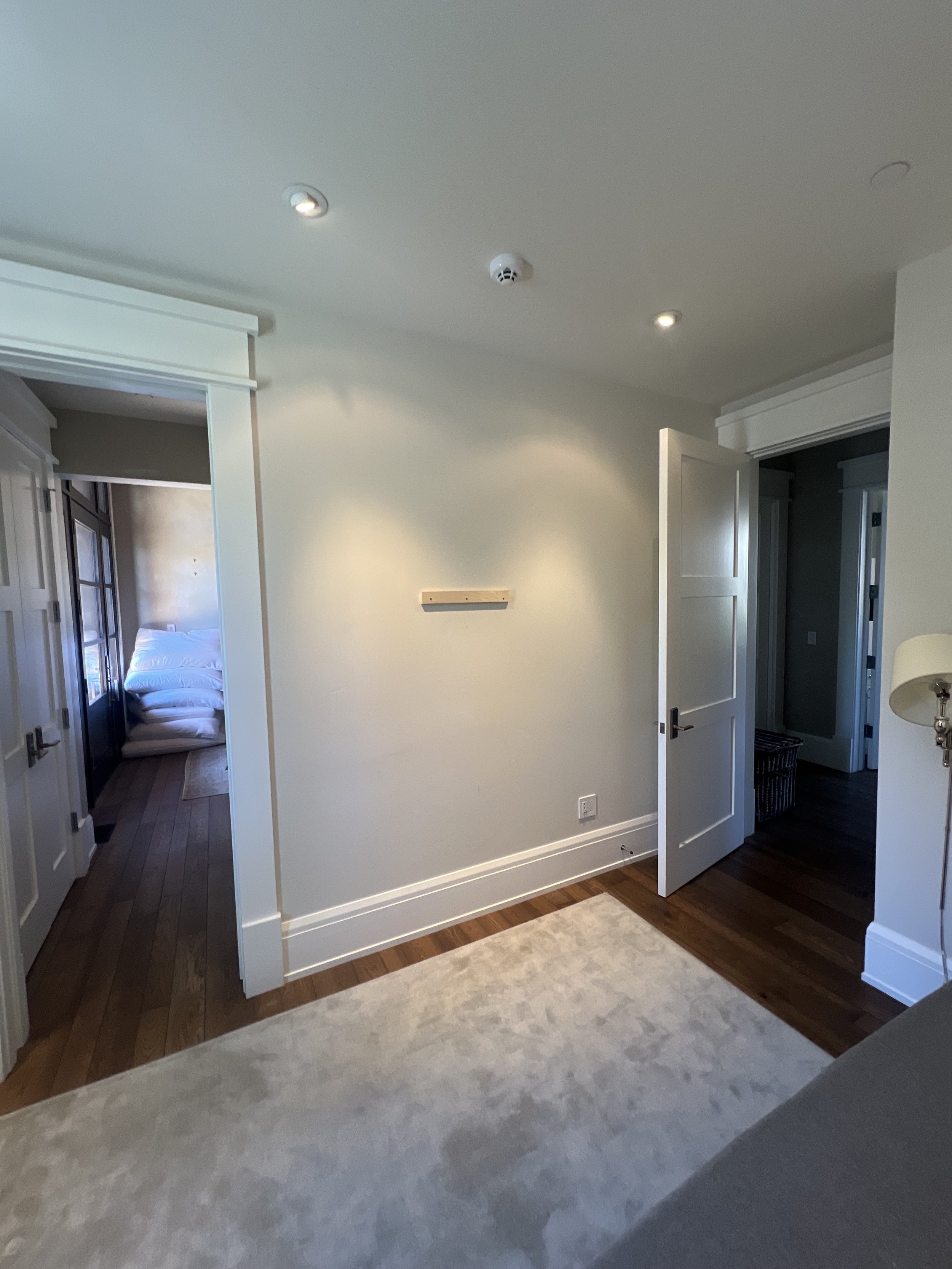 Interior of a room with a light carpet, white walls, and open doors. Recessed ceiling lights and smoke detector visible.