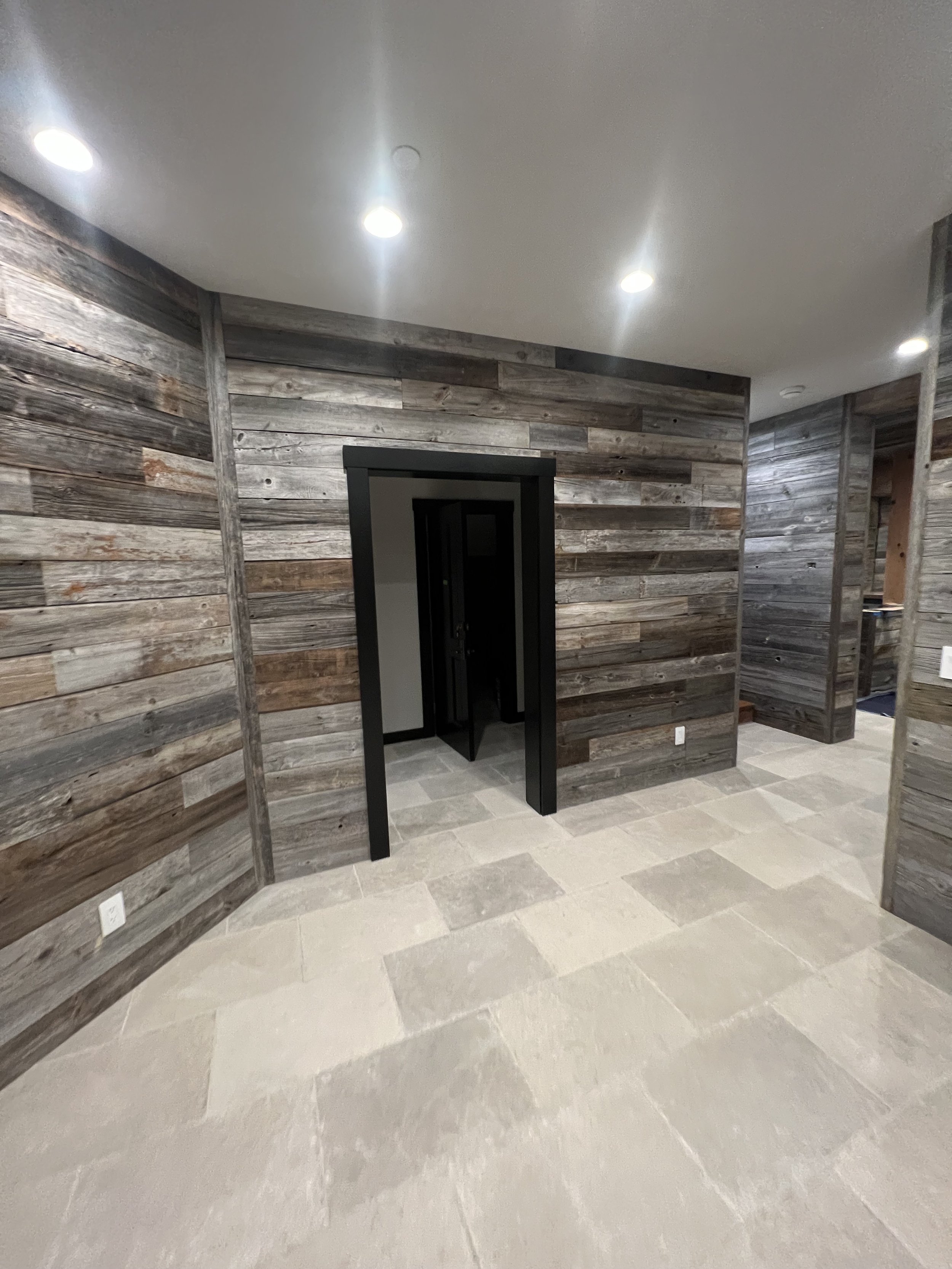 Room with grey wood paneled walls and light stone tile floors