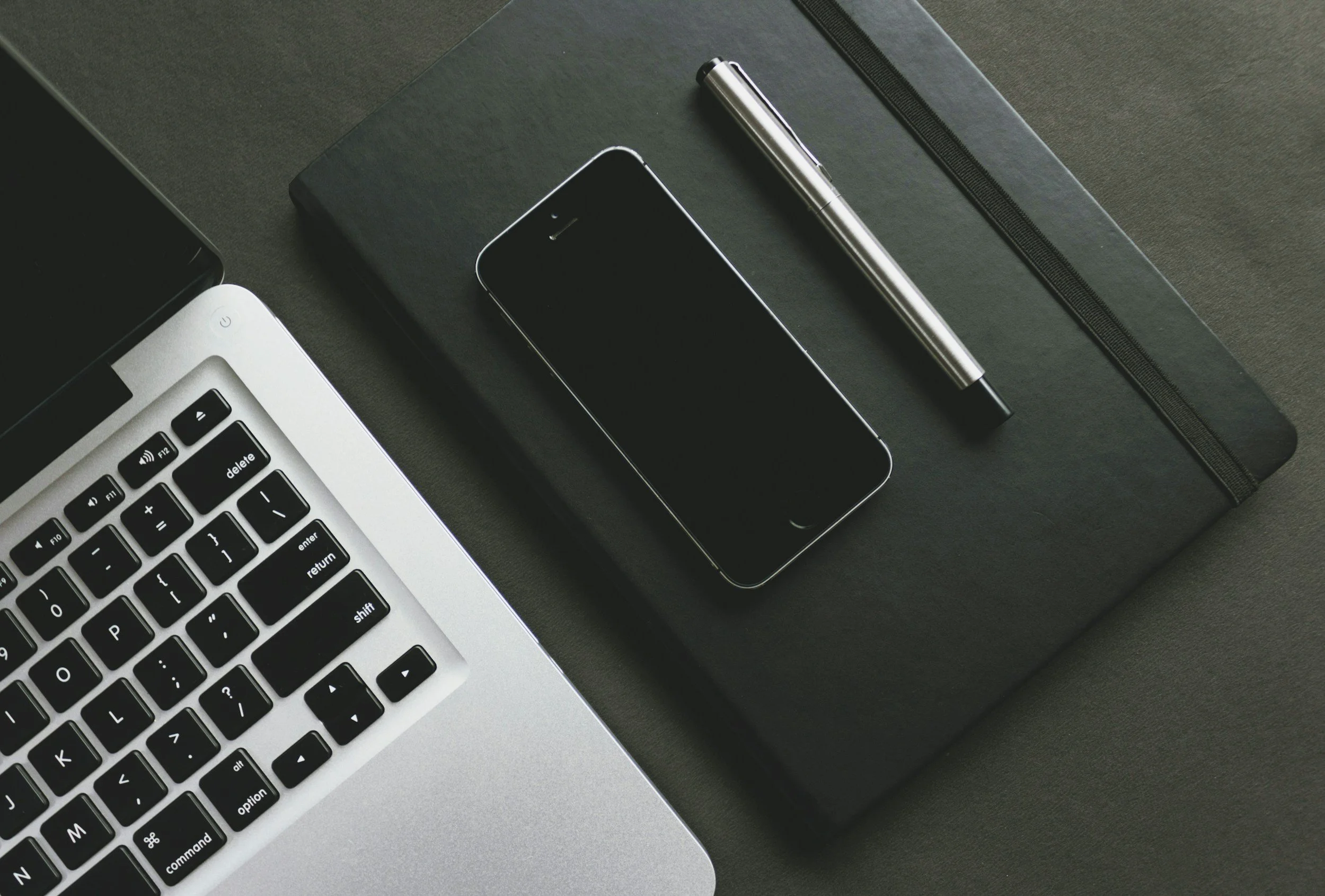 Desk with a laptop, smartphone, notebook, and pen.