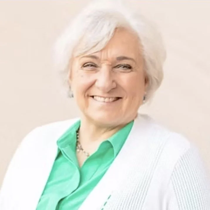 A smiling woman with short white hair, wearing a light green blouse and white blazer.