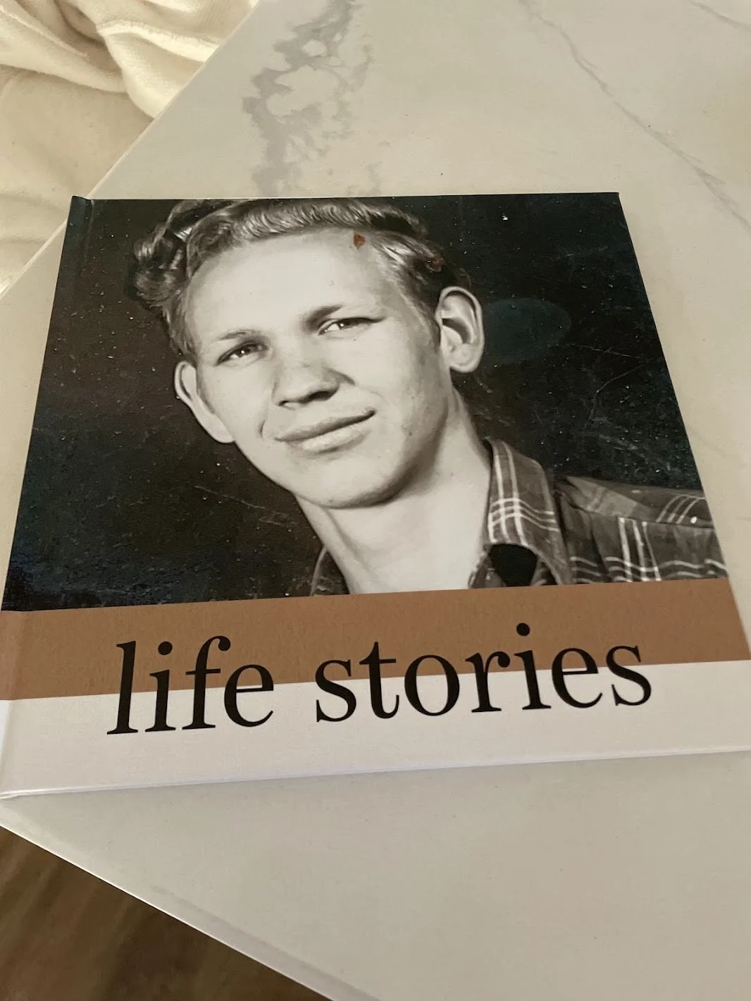 A book cover with a black-and-white photo of a young man with wavy hair, wearing a plaid shirt. The title is "life stories" in lowercase letters.