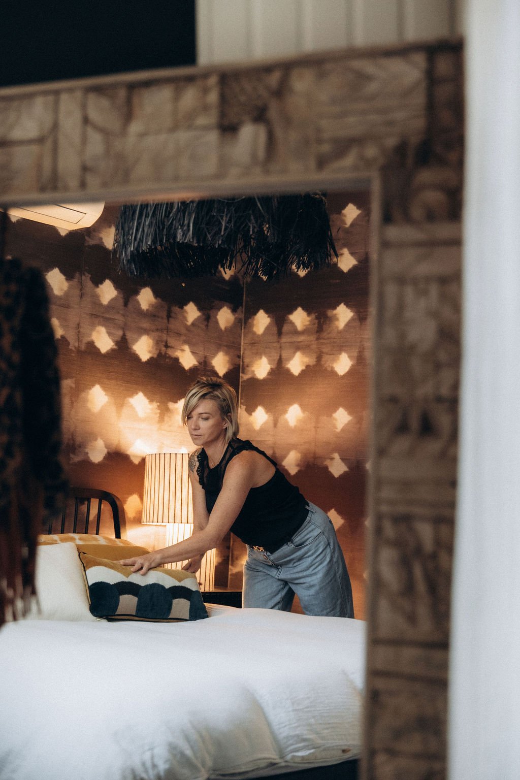 Une femme changeant la literie dans une chambre décorée avec un mur en bois et un lampadaire.